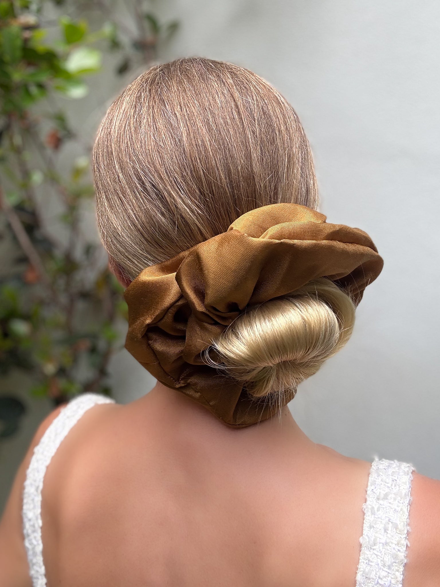 Woman with a large brown scrunchie in her hair against a blurred natural background