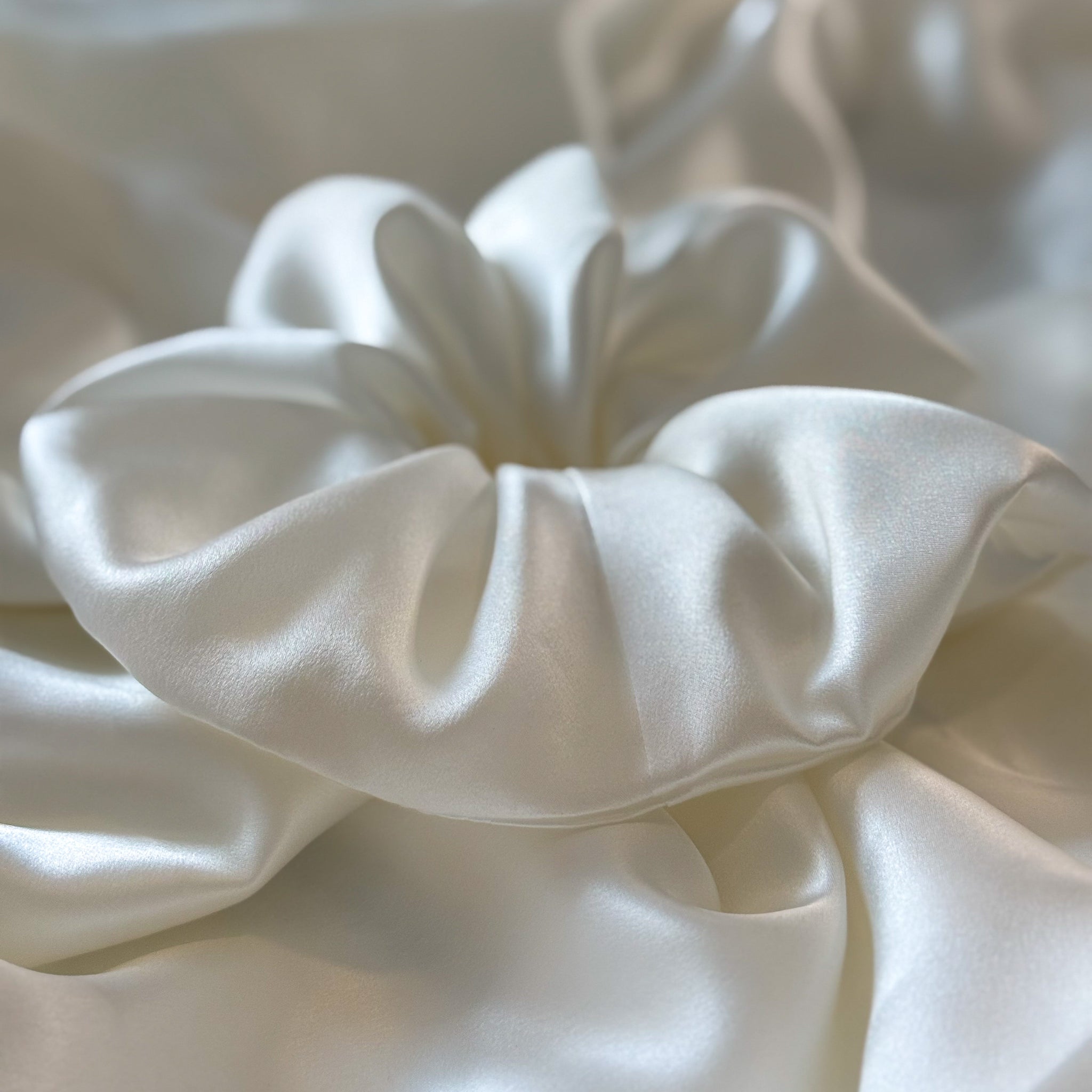 Close-up of a white satin scrunchie with a blurred background