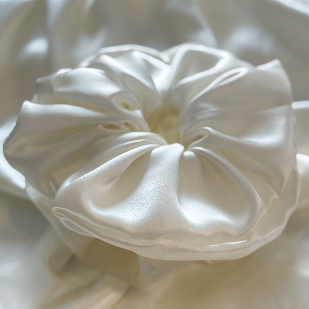 Close-up of a white satin hair scrunchie on a matching fabric background