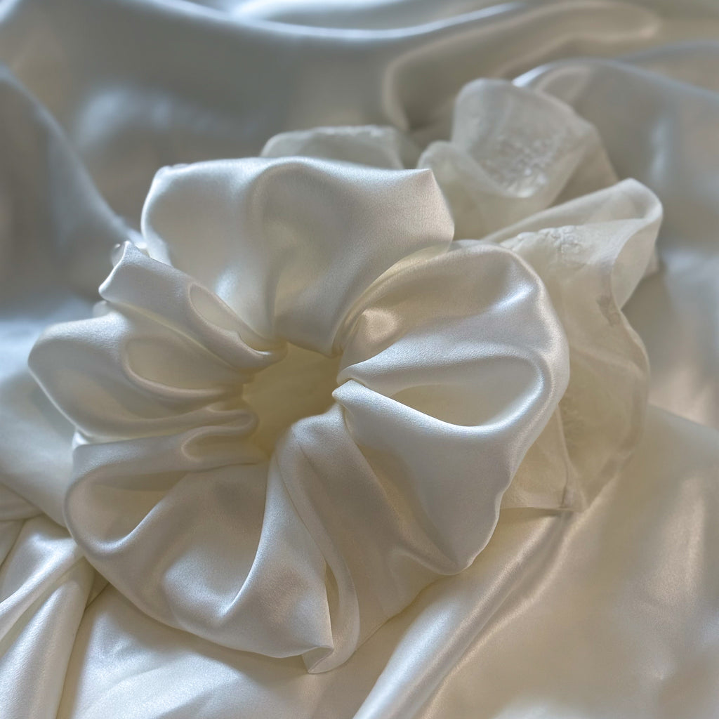 White satin scrunchie on a textured white fabric background