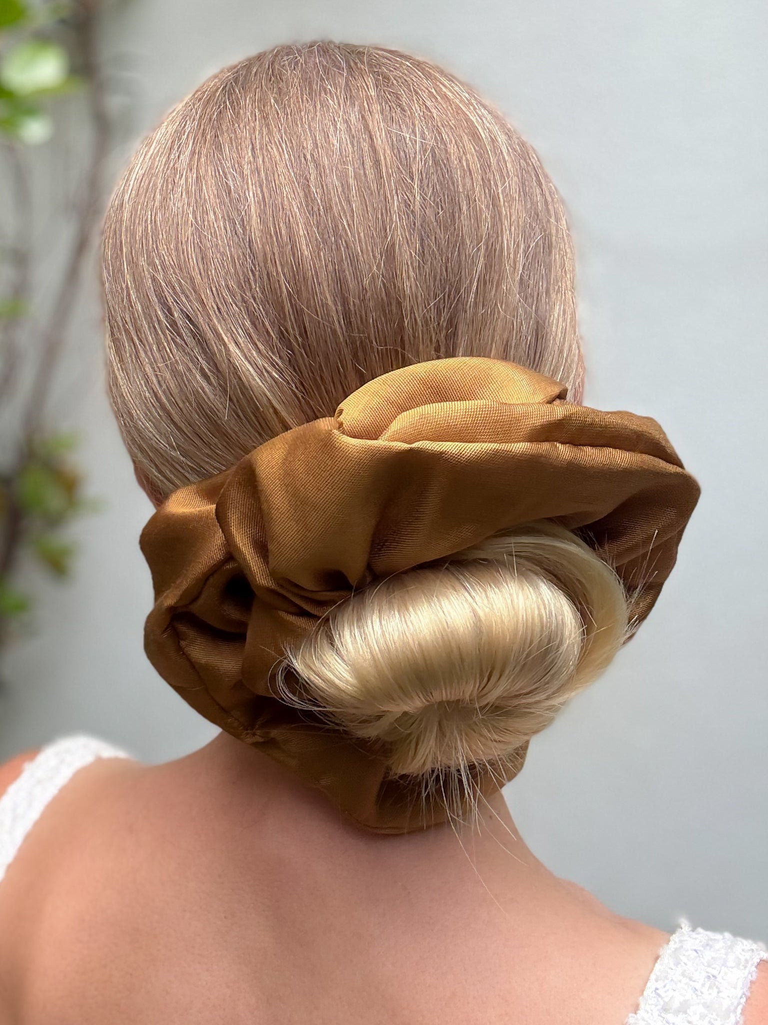Person with a large brown scrunchie in their hair against a light background
