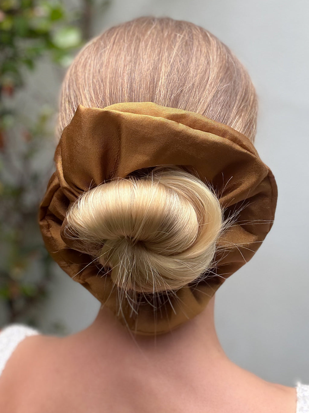 Person with blonde hair styled in a bun covered by a brown scrunchie against a neutral background