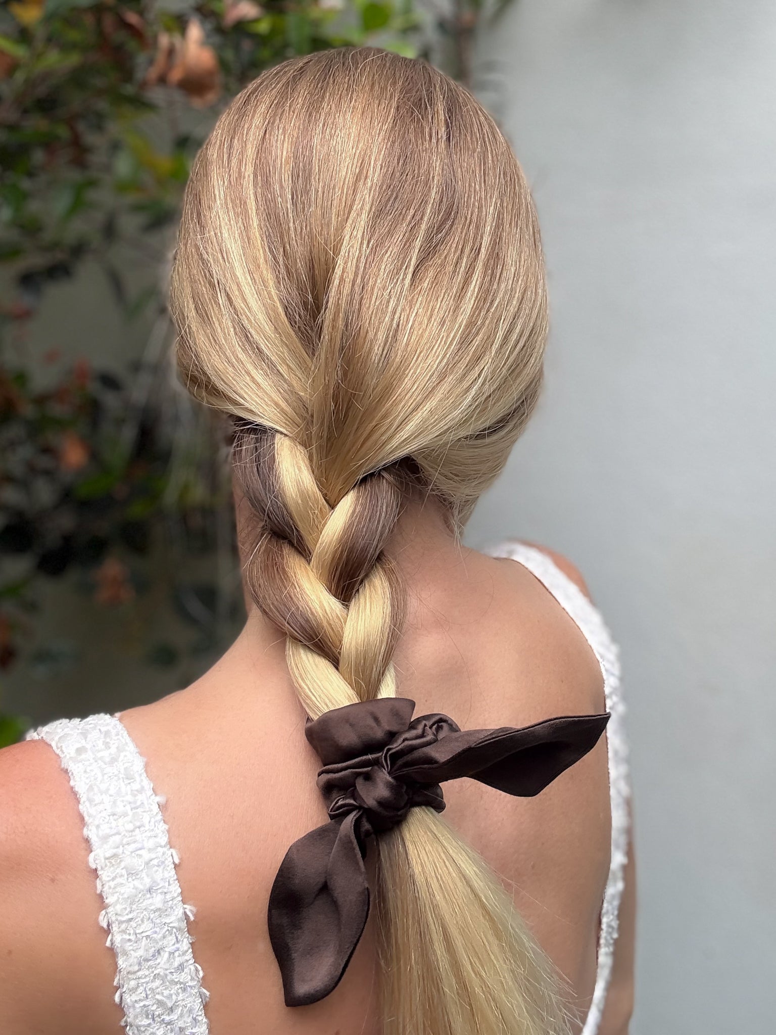 Person with braided hair wearing a white top, with a blurred natural background