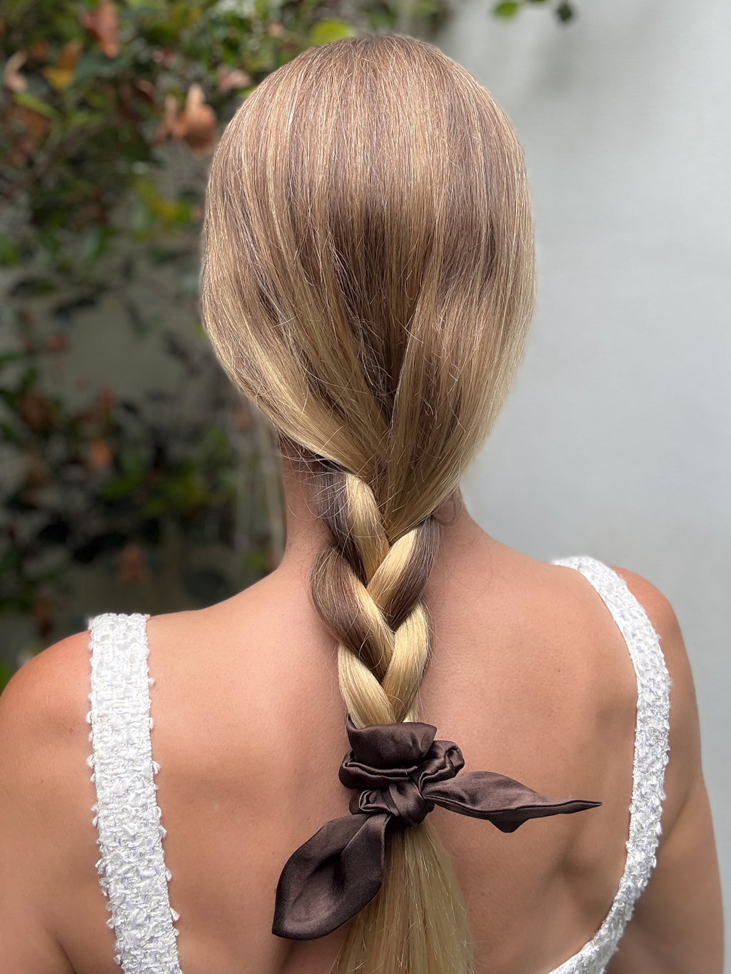 Person with braided hair wearing a white top, standing outdoors.