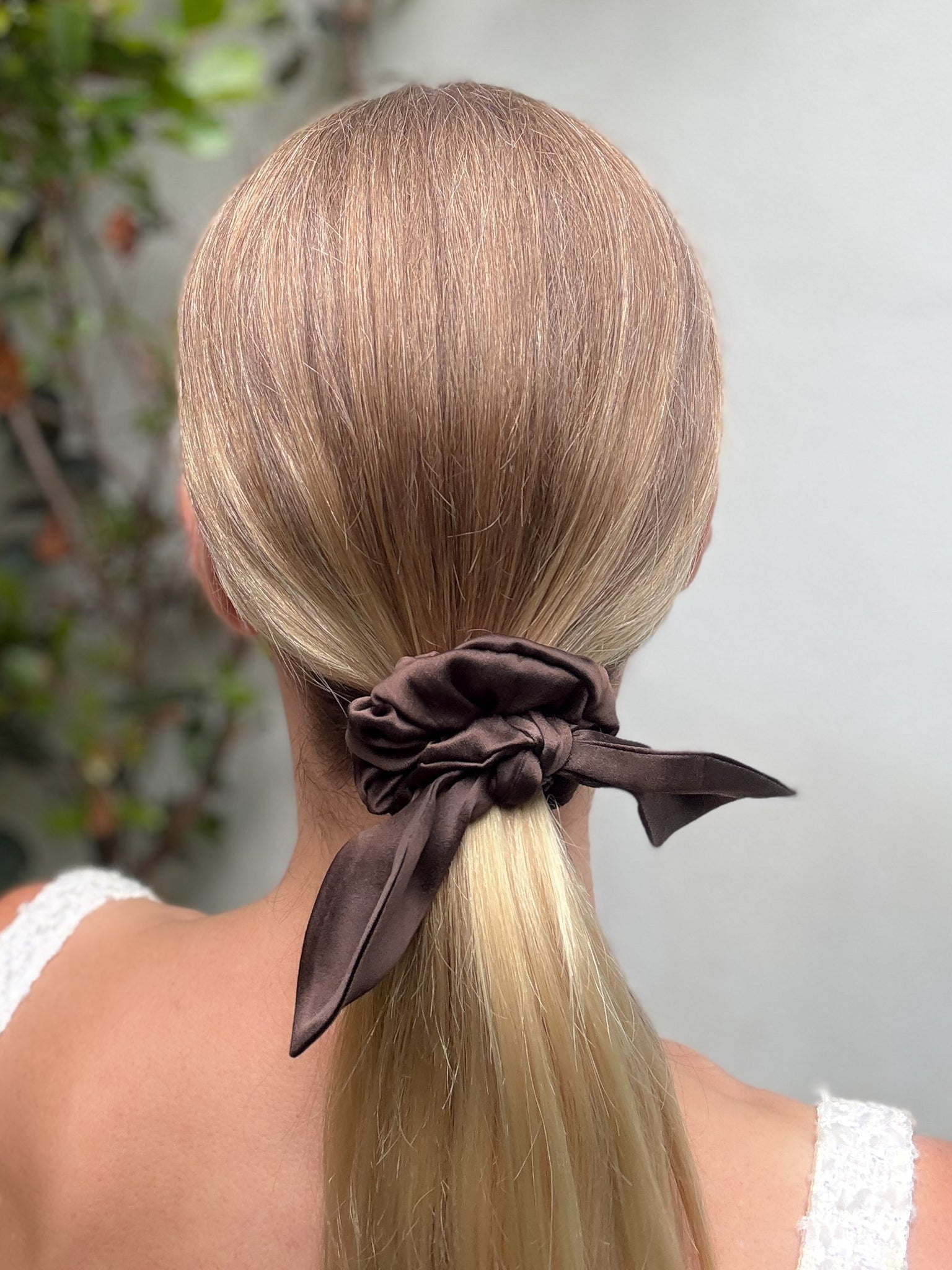 Blonde hair tied into a ponytail with a brown scrunchie against a neutral background