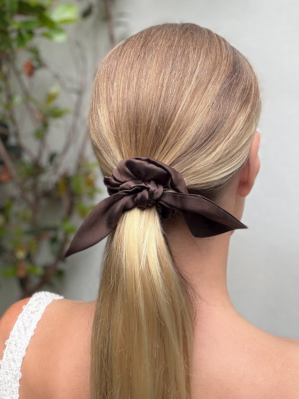 Woman with blonde hair tied in a ponytail with a brown scrunchie, outdoor setting