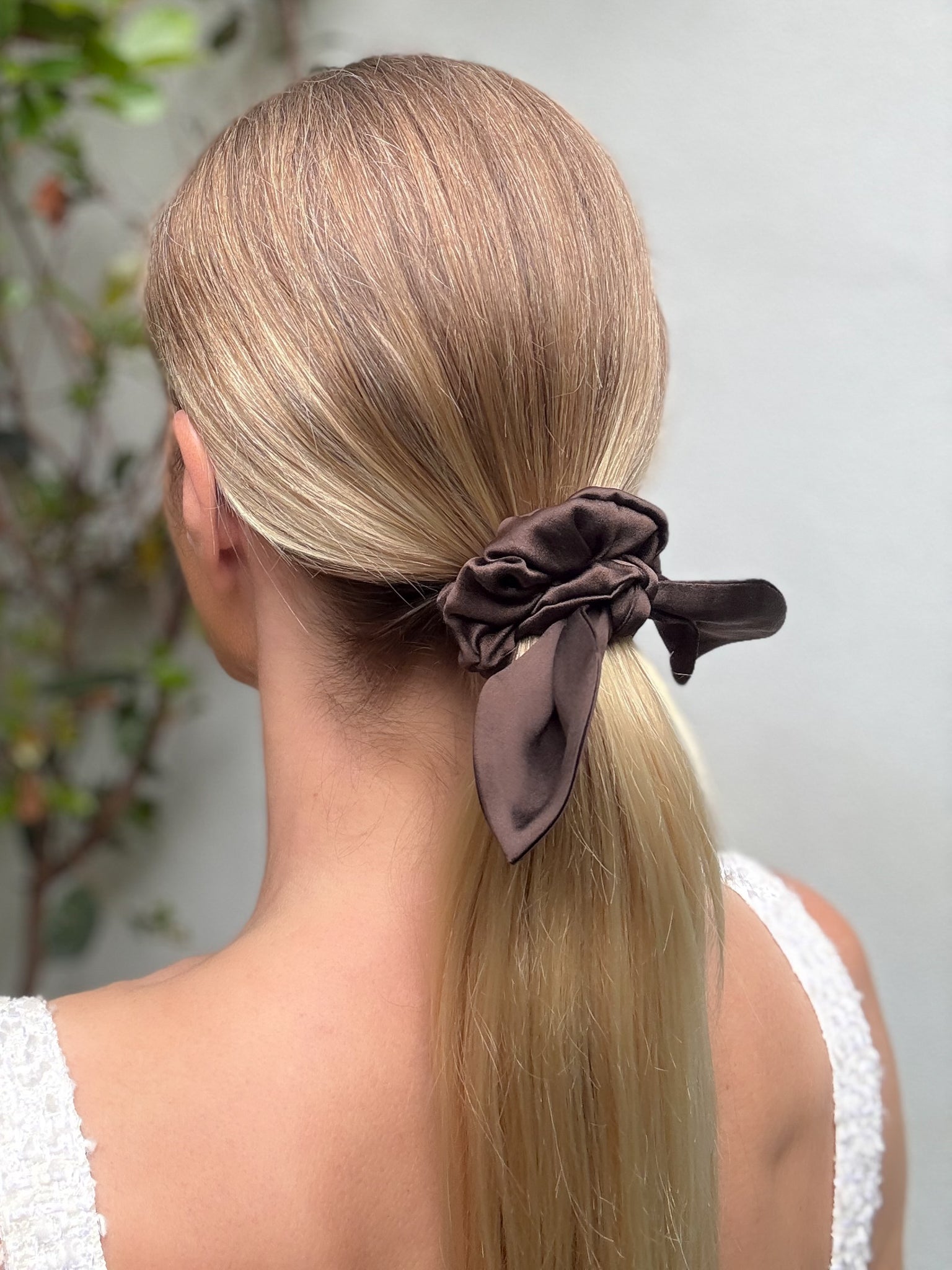 Woman with a low ponytail held by a brown scrunchie against a neutral background