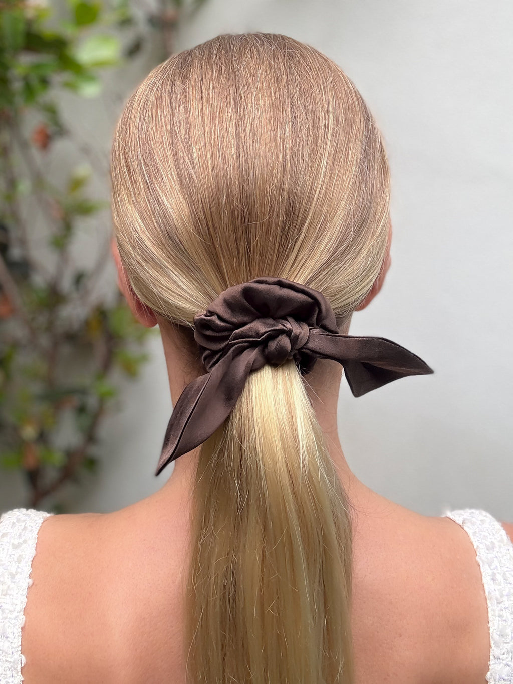 Blonde hair tied into a ponytail with a brown scrunchie against a neutral background