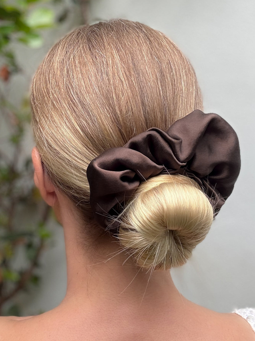 Brown scrunchie on a bun with a blurred natural background