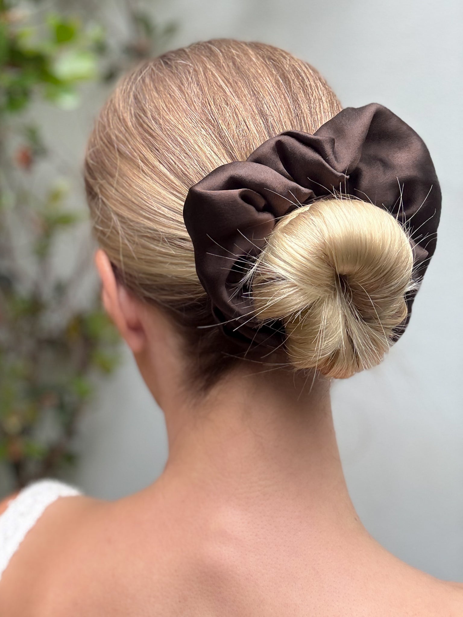 Brown scrunchie on a bun with a blurred natural background