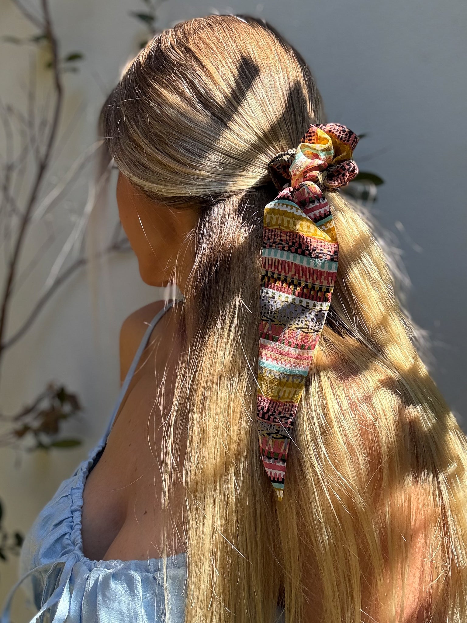 Person with long blonde hair tied with a colorful patterned scrunchie against a neutral background
