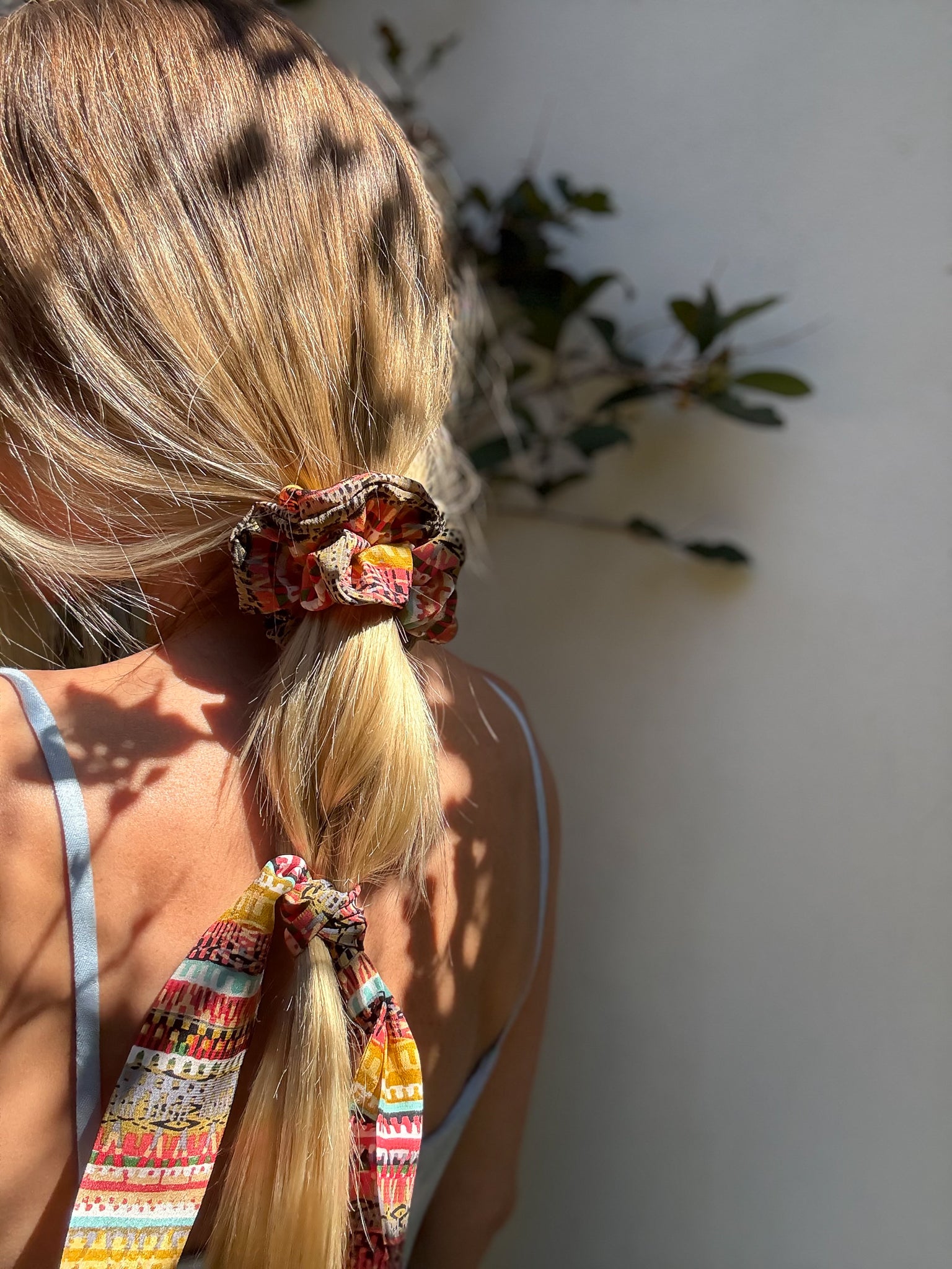Person with colorful scrunchies in a ponytail against a neutral background
