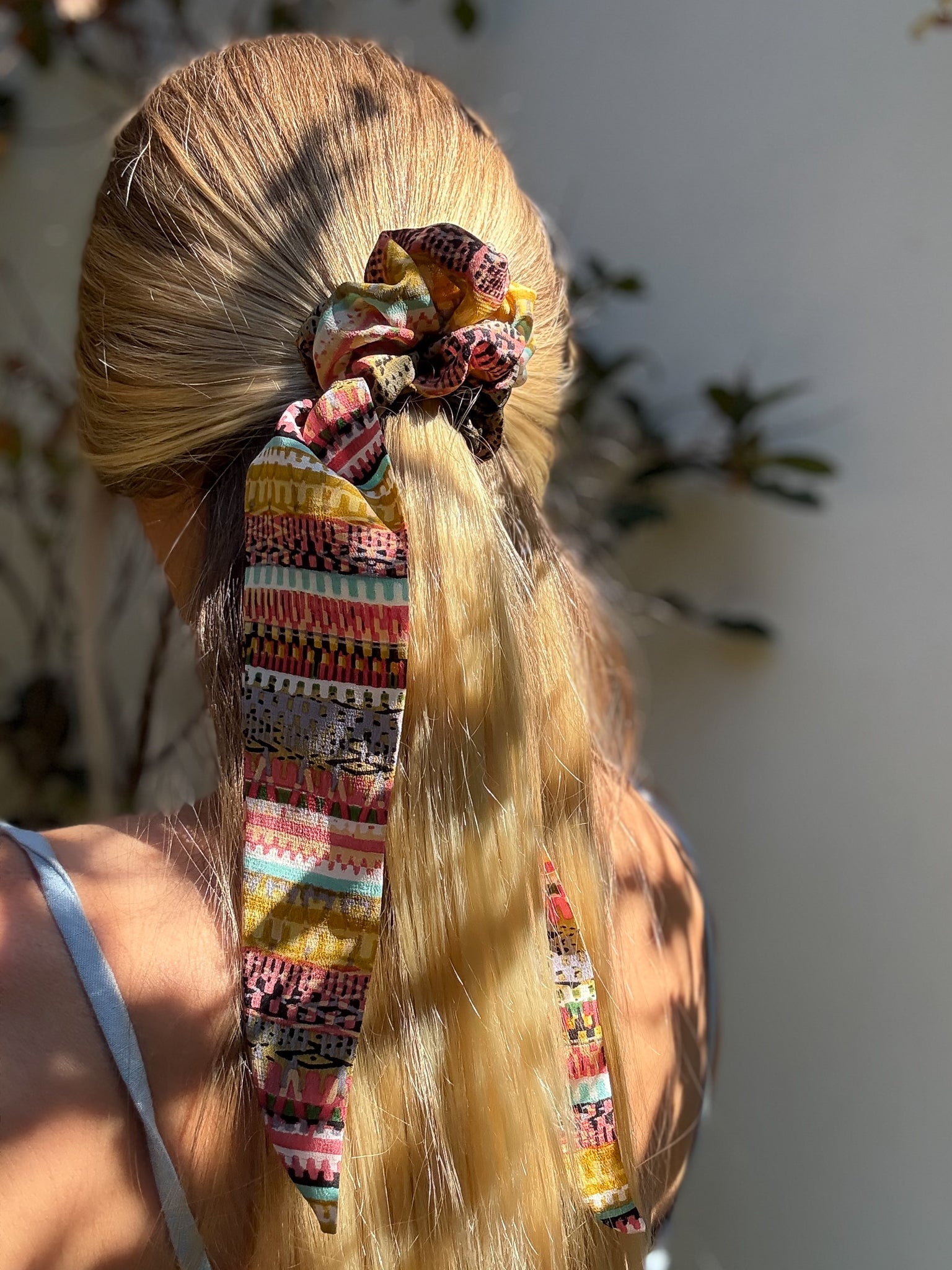 Colorful scrunchies in a person's hair with a blurred natural background