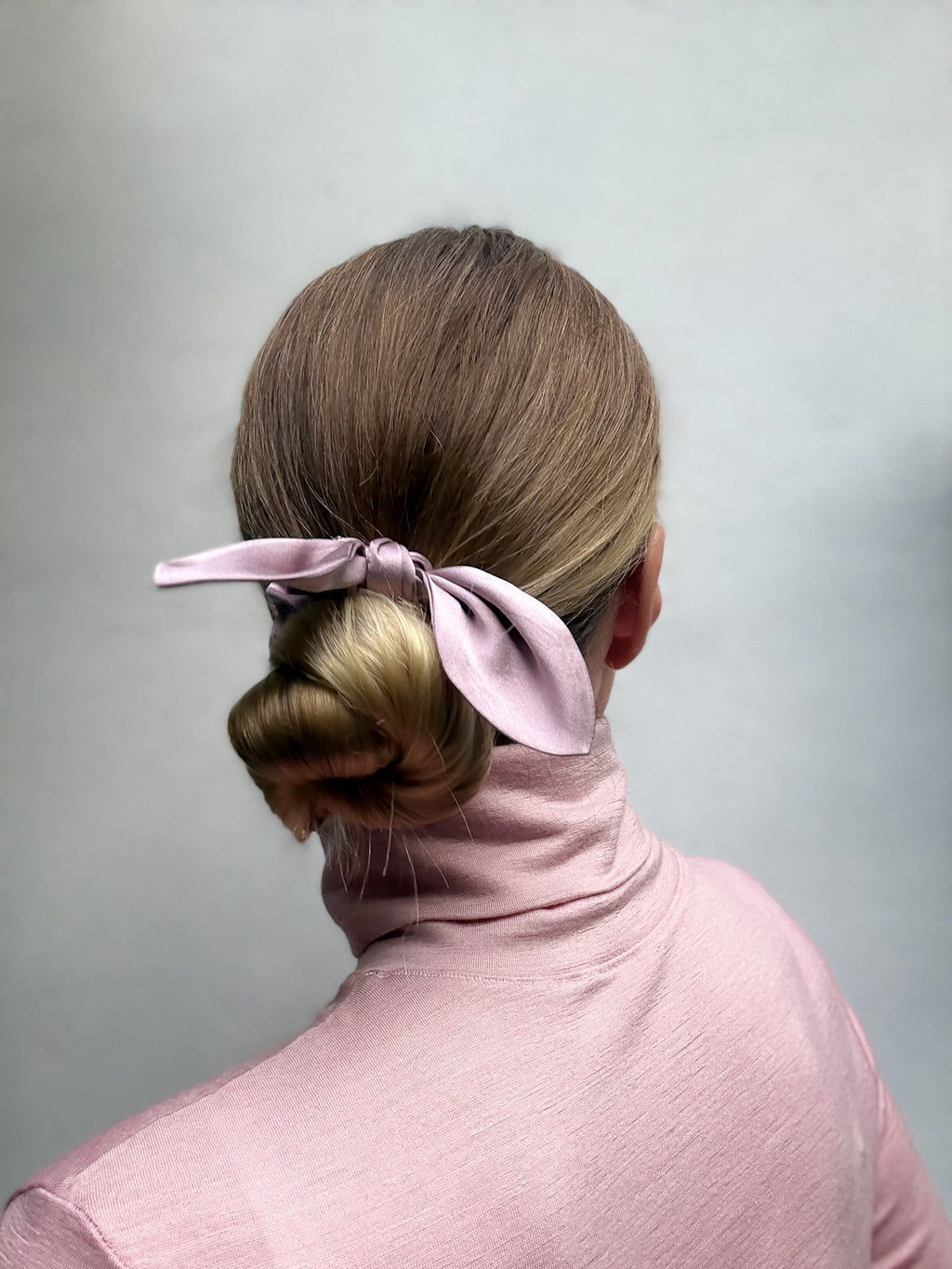 Person with a bun and silk bow scrunchie against a gray background