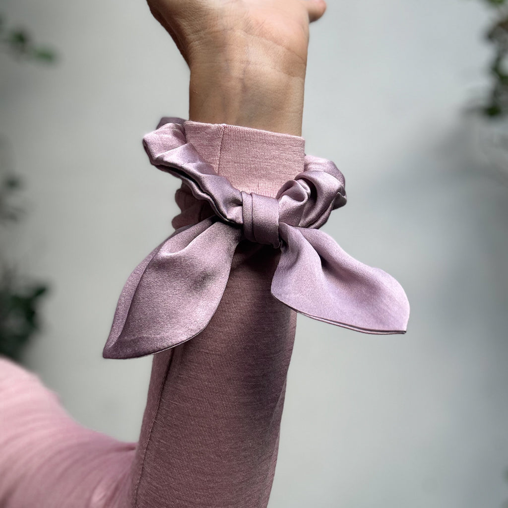 Pink scrunchie wrapped around wrist on a blurred background