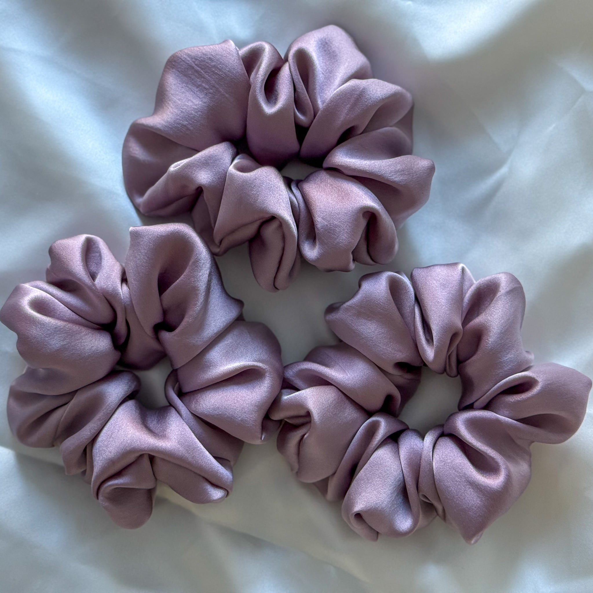 Three purple scrunchies on a white fabric background