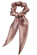 Rose gold satin scrunchie with a long bow on a light gray background
