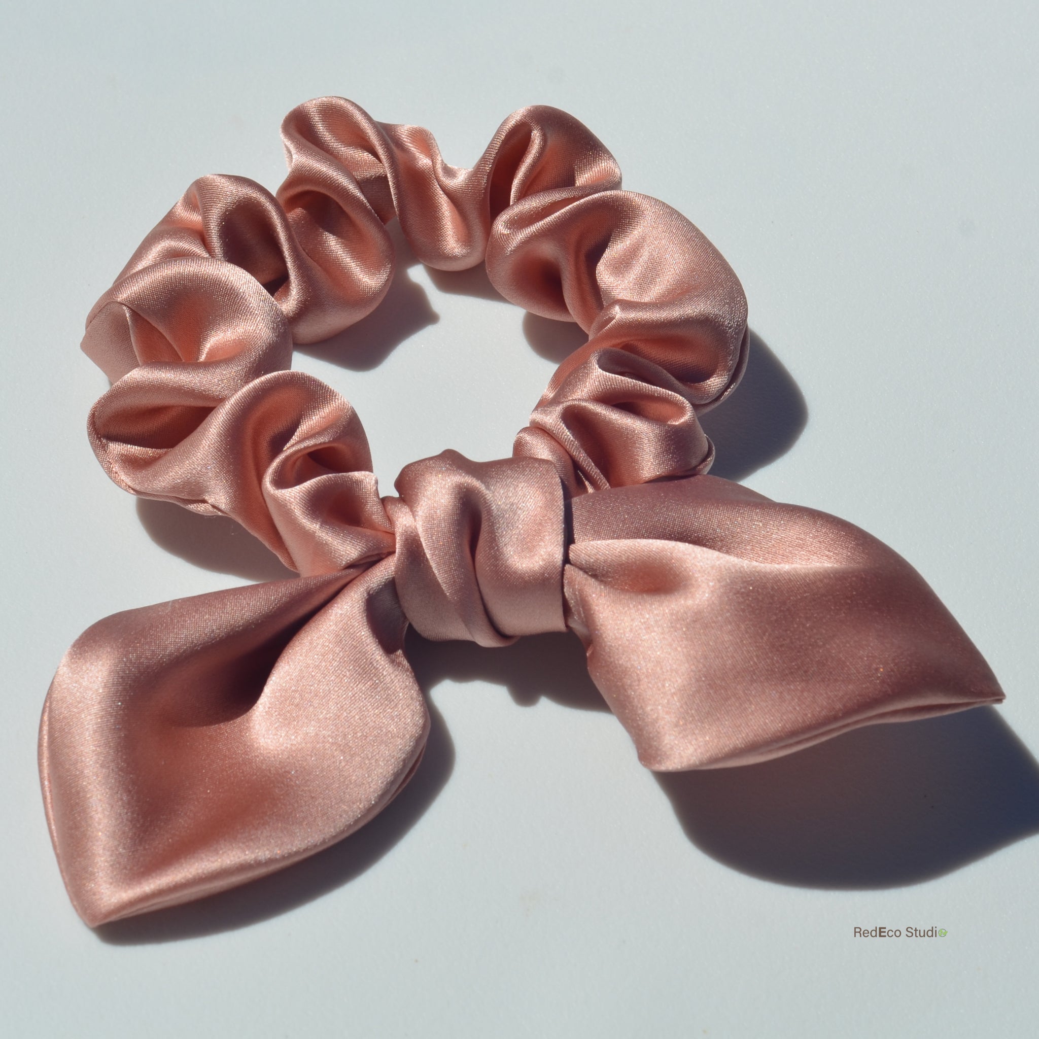 Pink satin scrunchie with a bow on a light gray background