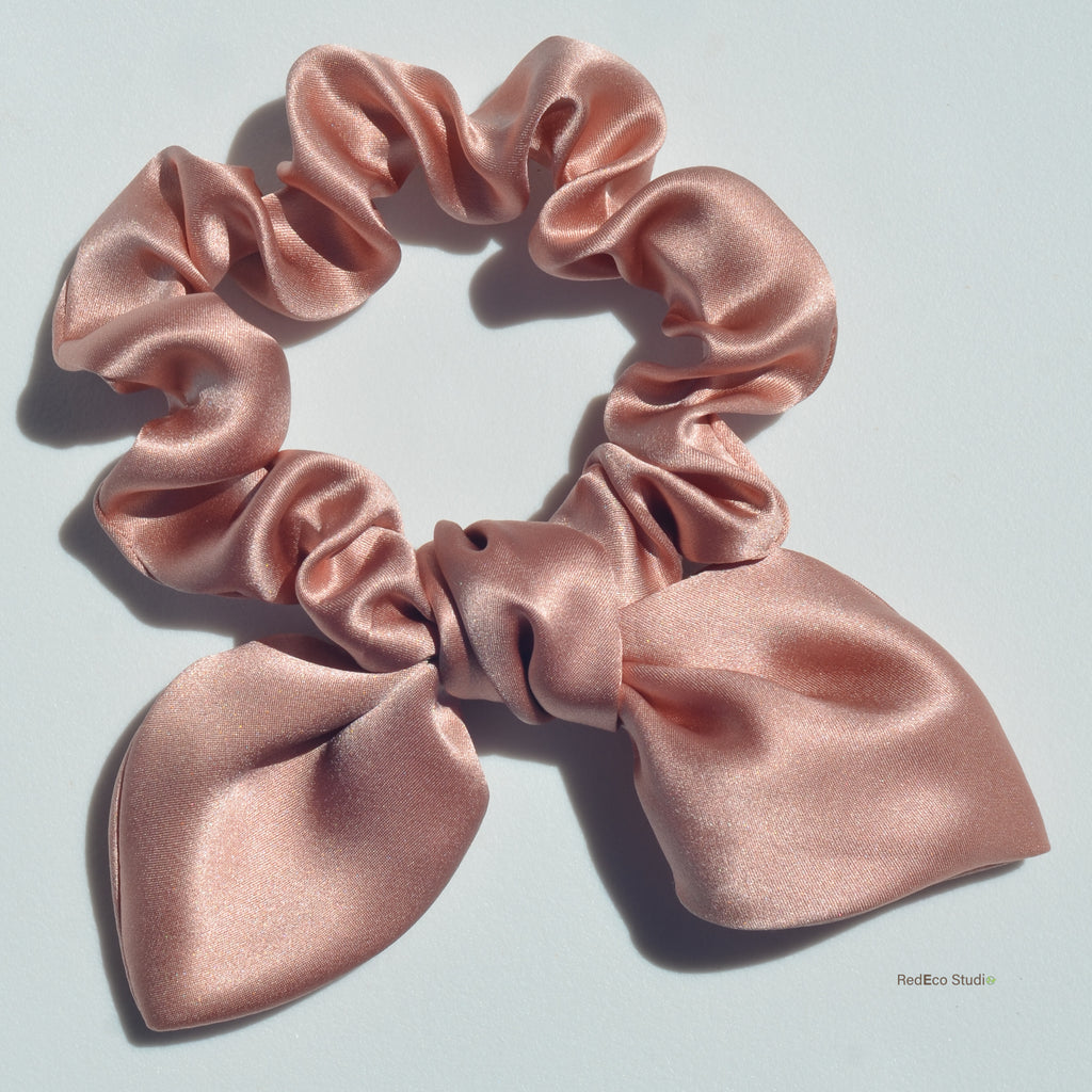 Pink satin scrunchie with a bow on a light gray background
