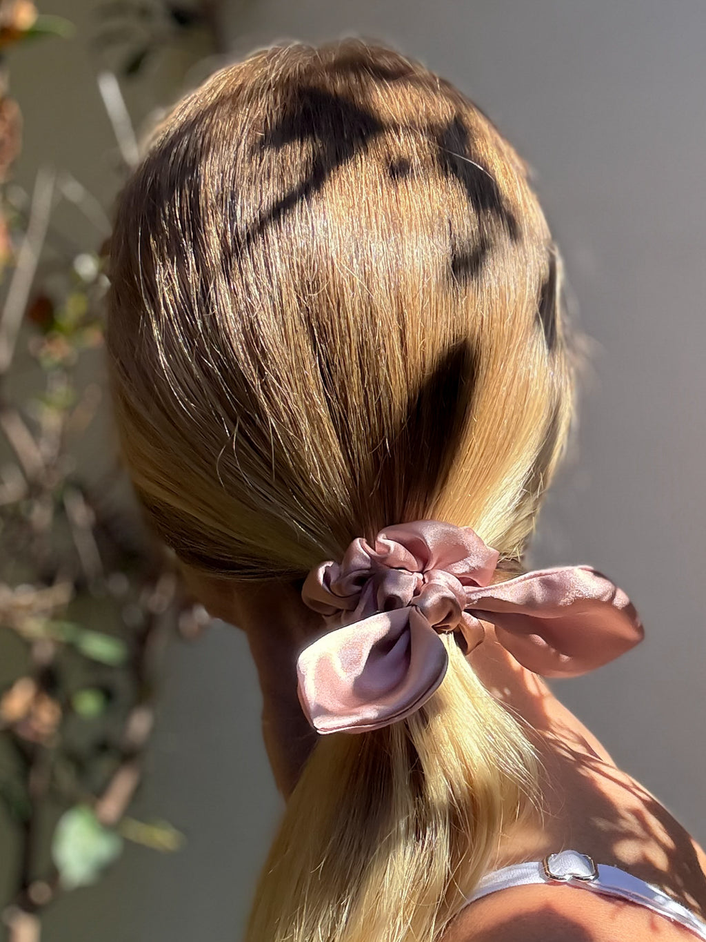 Blonde hair tied with a pink scrunchie against a neutral background
