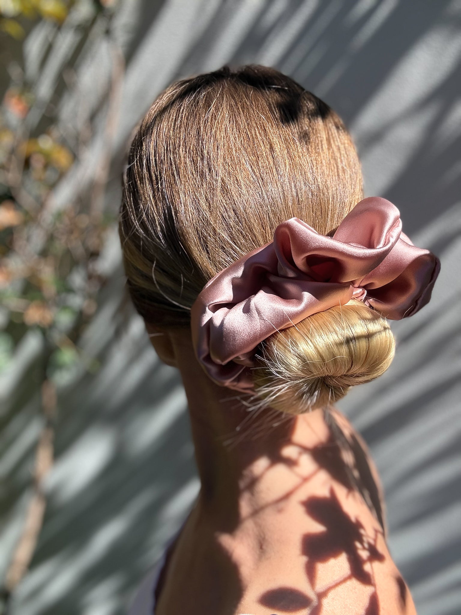 Person with a stylish hairdo and pink scrunchie against a natural background