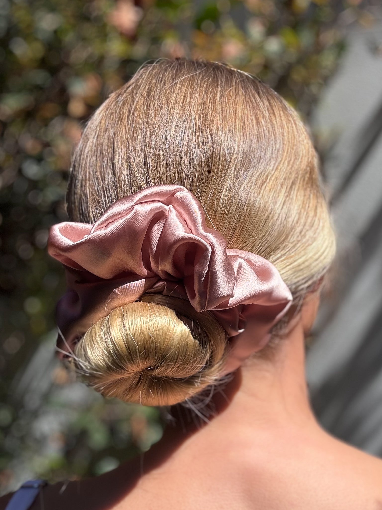 Pink scrunchie on a bun with blurred natural background