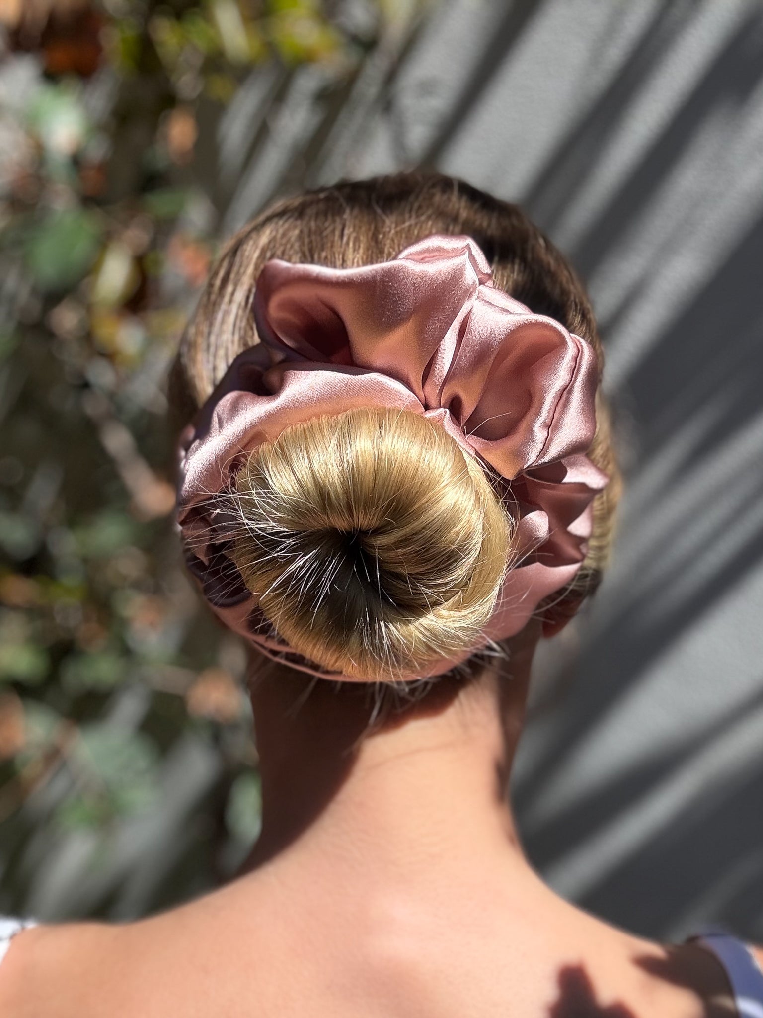 Person with a bun held in place by a pink satin scrunchie, outdoors.