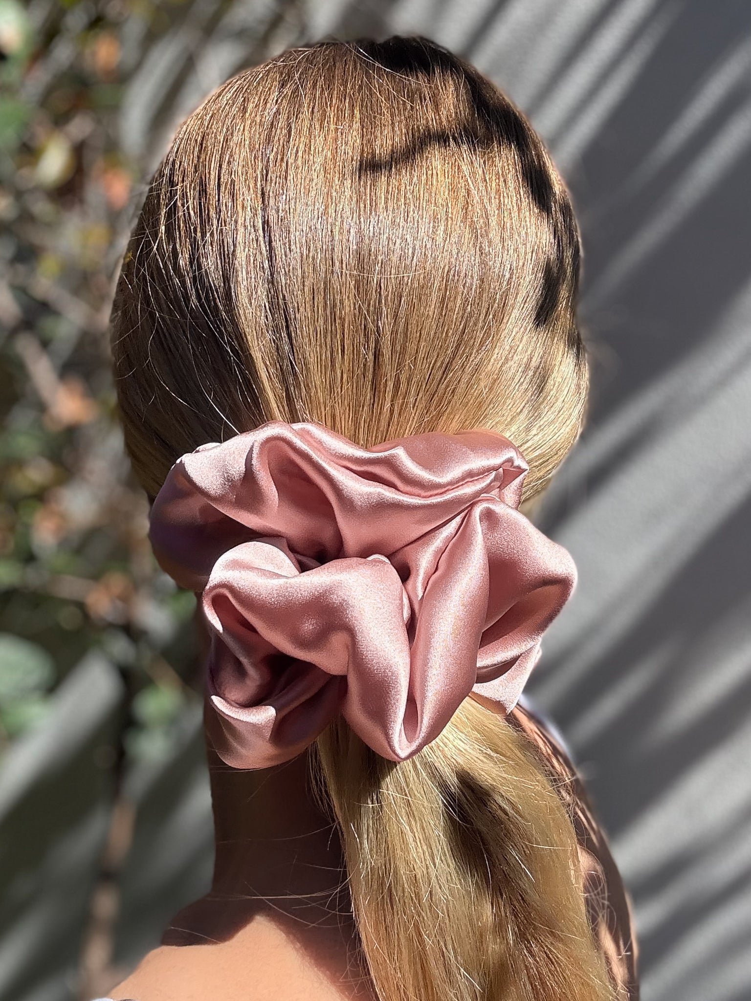 Pink scrunchie in a person's hair with a blurred natural background