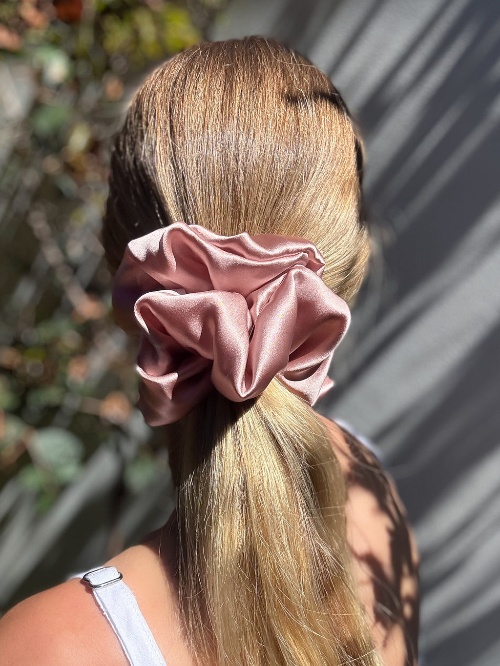 Person with a pink scrunchie in their hair, standing outdoors.