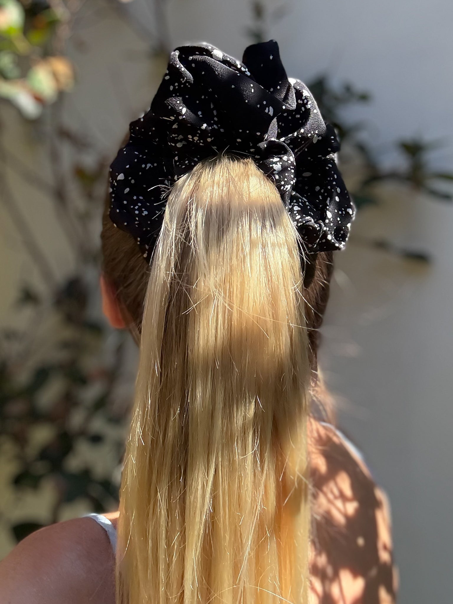 Person with long blonde hair wearing a black scrunchie outdoors.