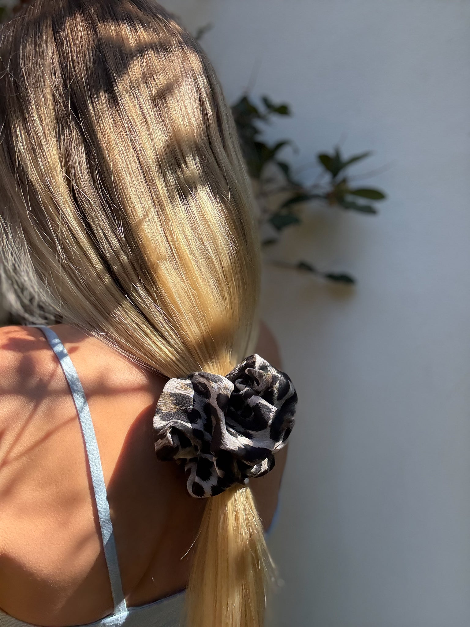 Person with blonde hair tied in a ponytail using a leopard print scrunchie, with a blurred background.