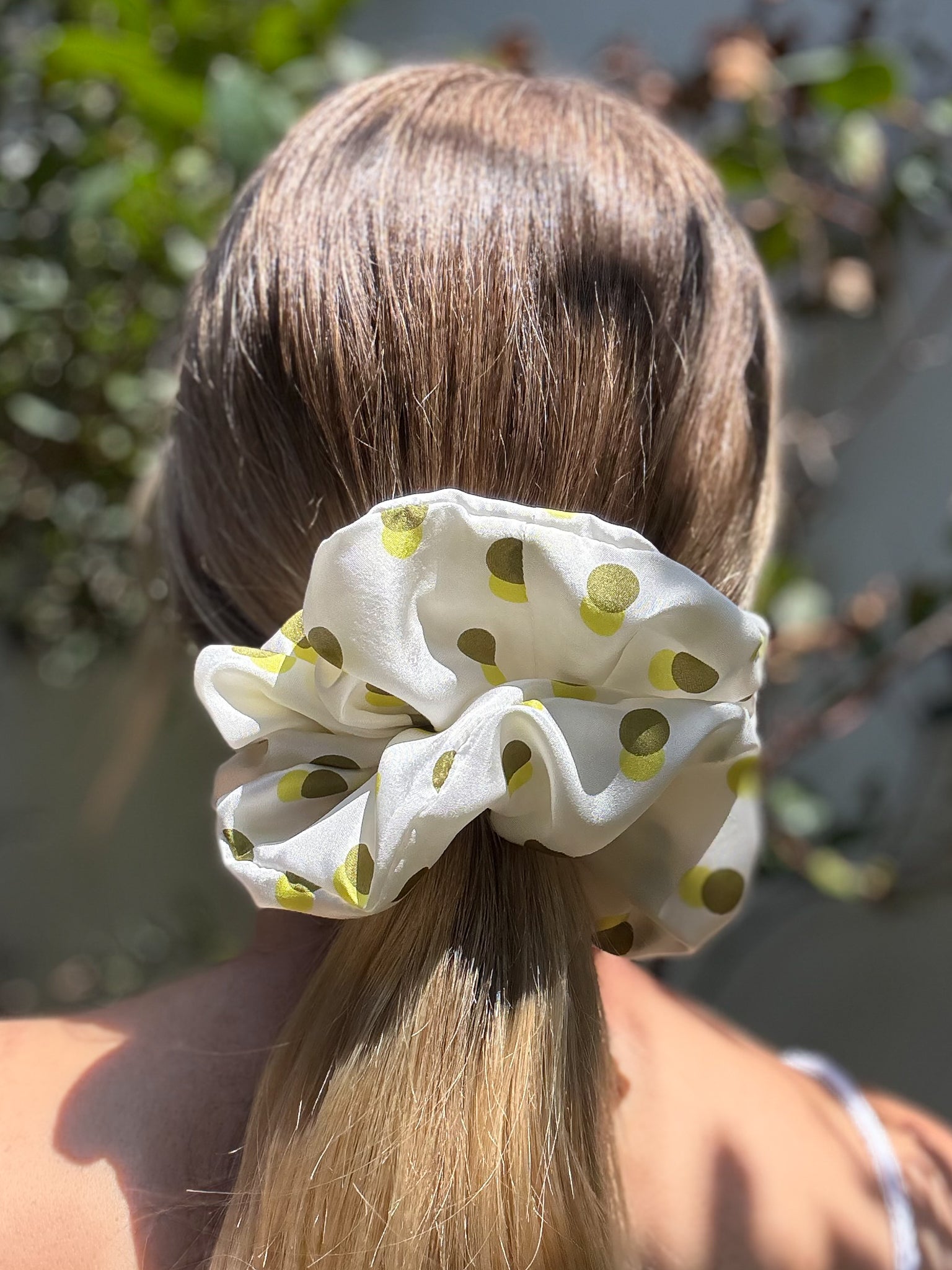 White scrunchie with green polka dots in a person's hair, outdoors.