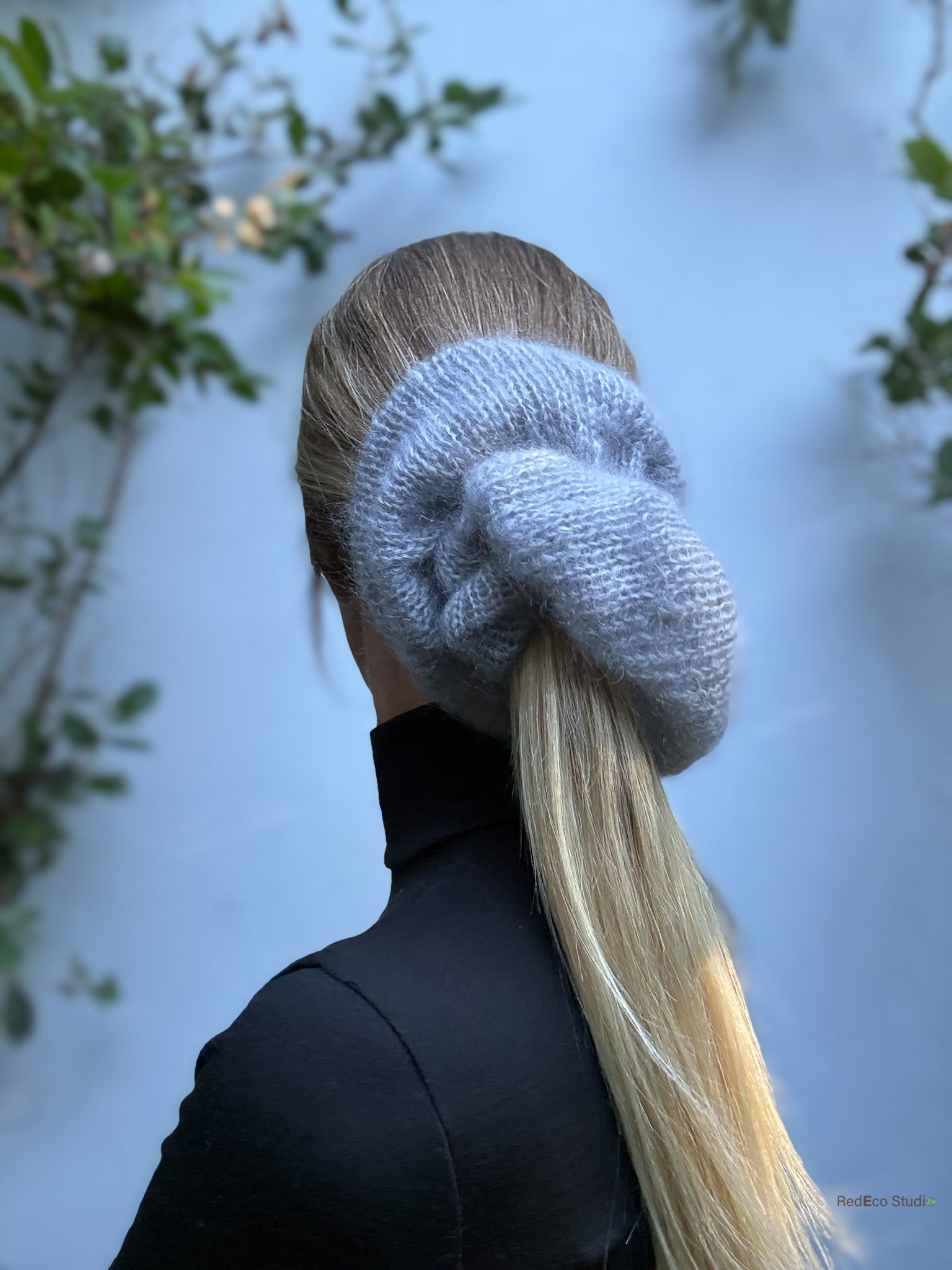 Person with an oversized knitted gray scrunchie in their hair against a light background