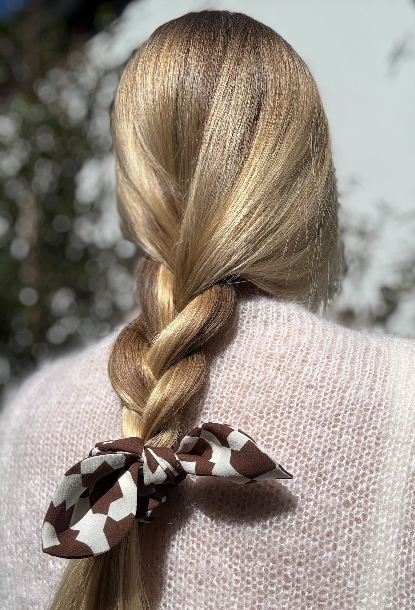 Person with braided hair tied with a brown and white silk scrunchie against a blurred natural background