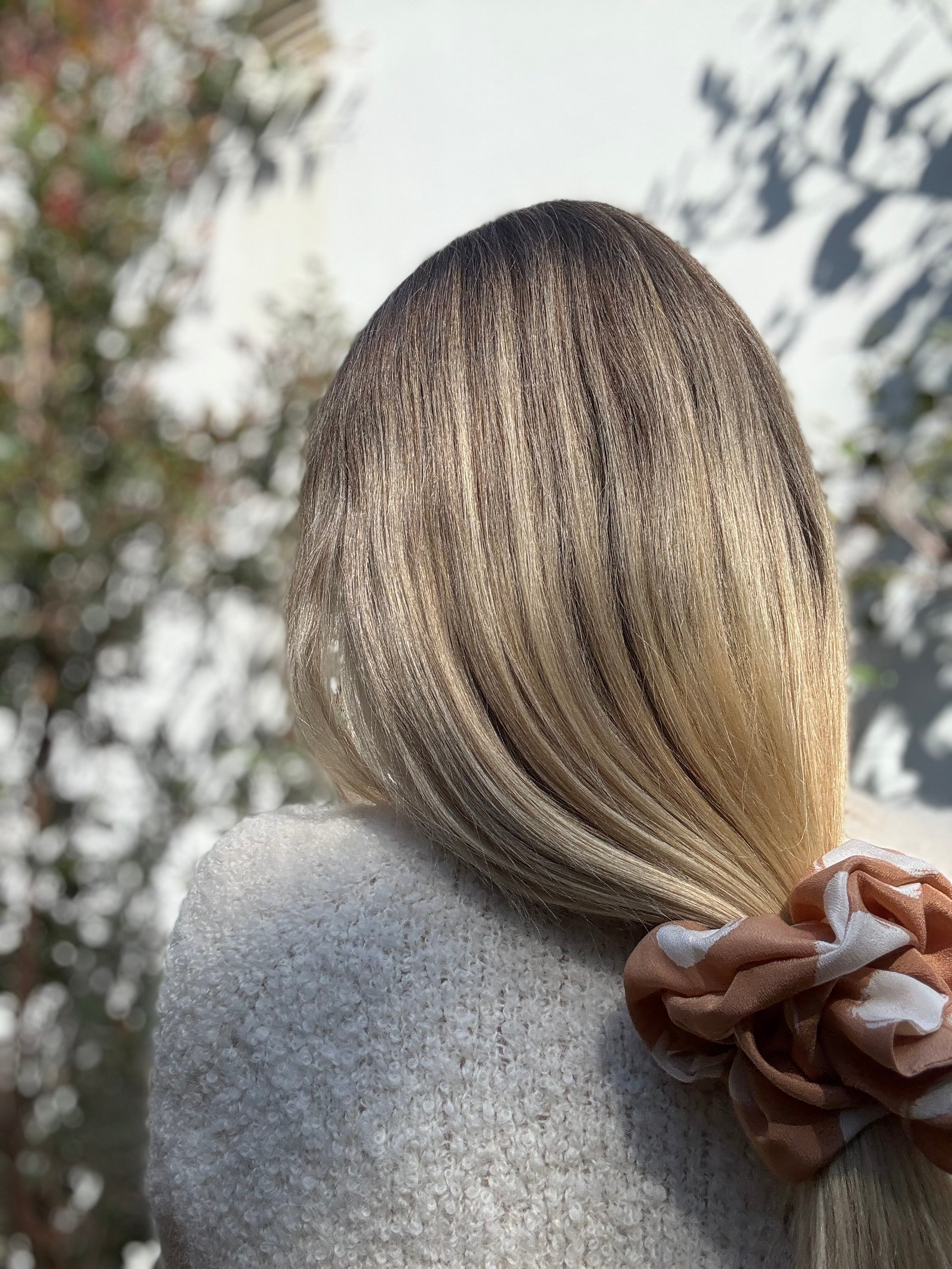 Person with blonde hair tied back with a silk scrunchie, blurred natural background