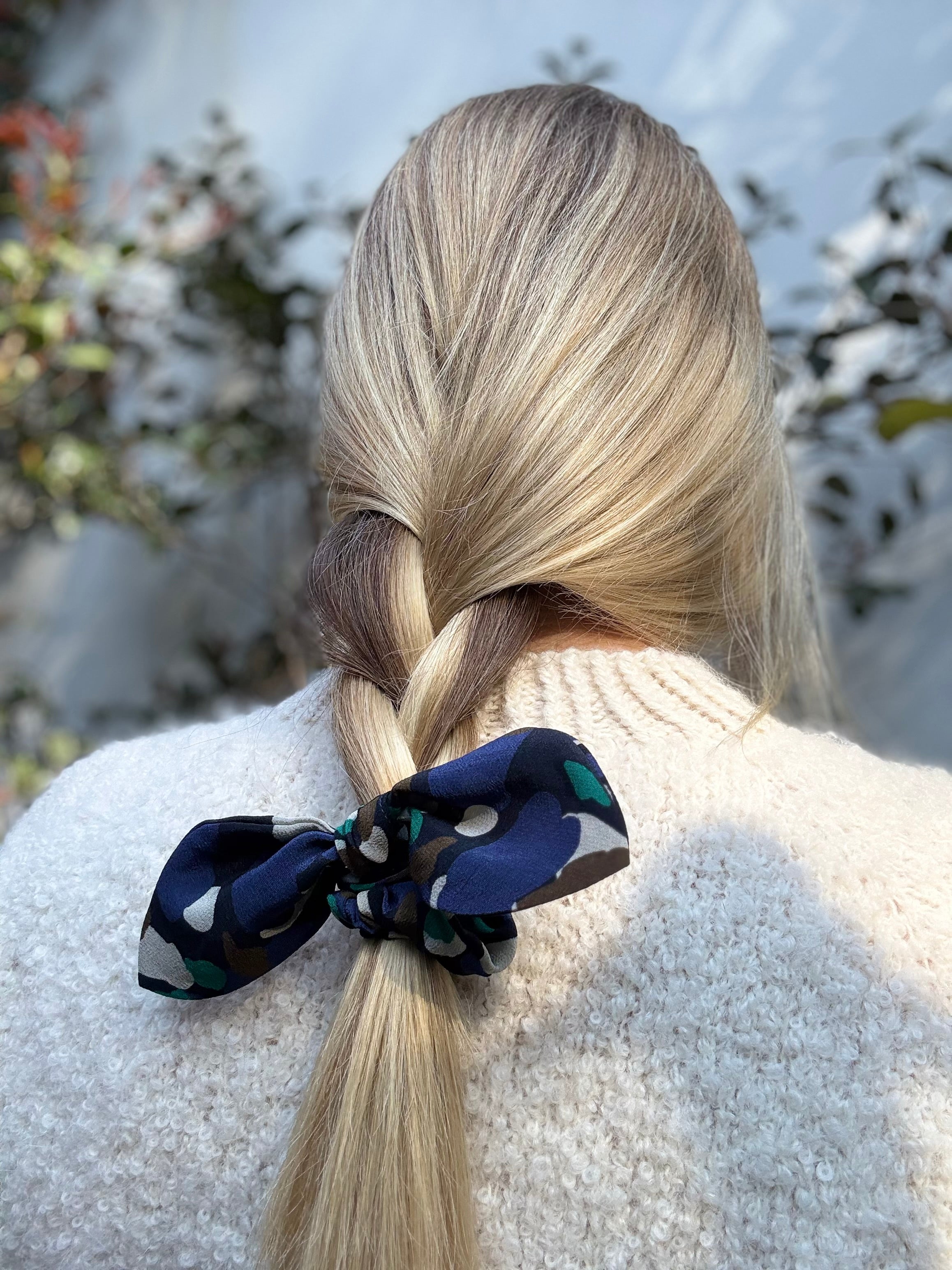 Person with blonde hair tied in a ponytail with a blue silk scrunchie featuring a geometric pattern.