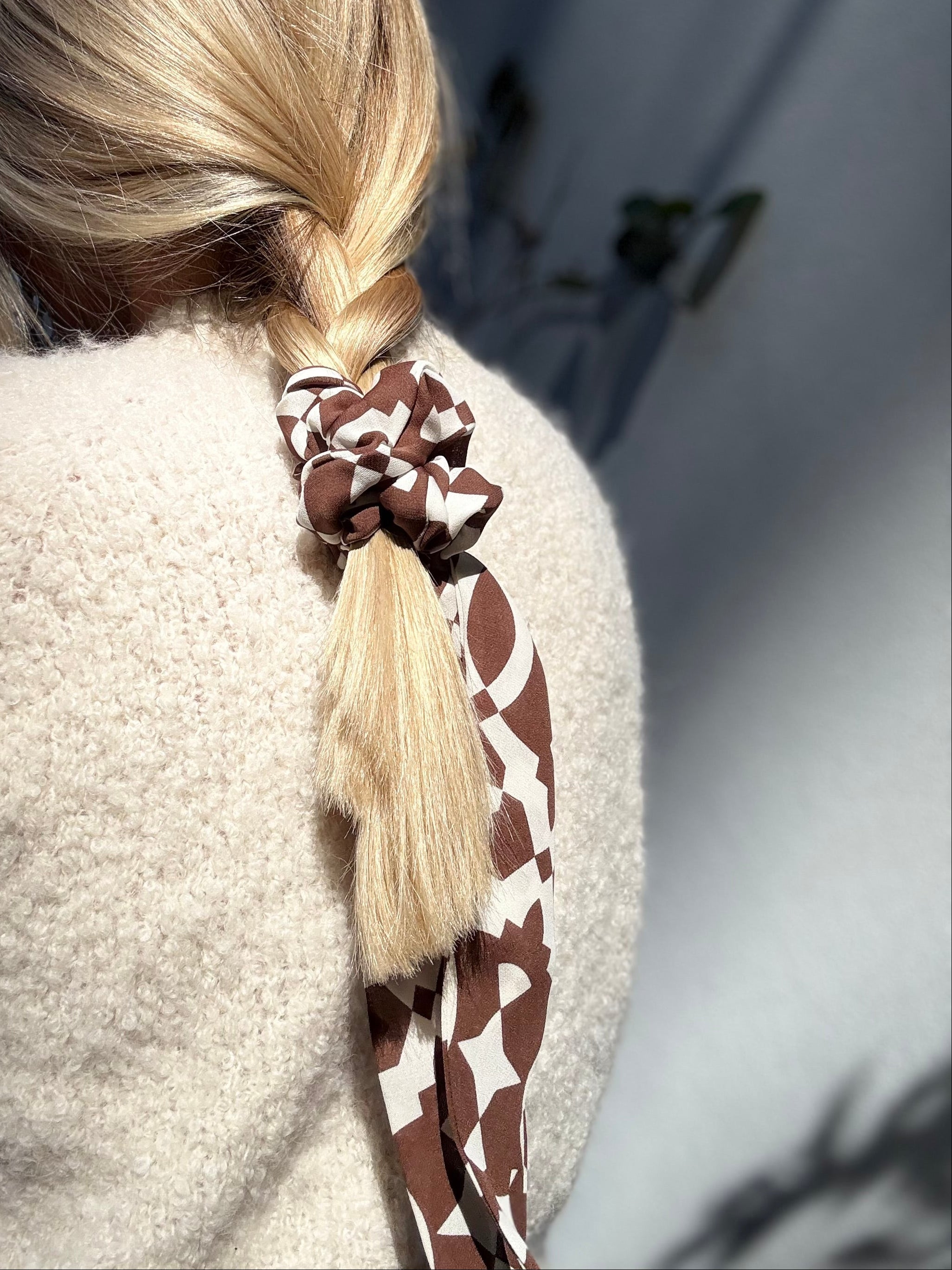 Close-up of a ponytail with a patterned silk scrunchie, blurred background