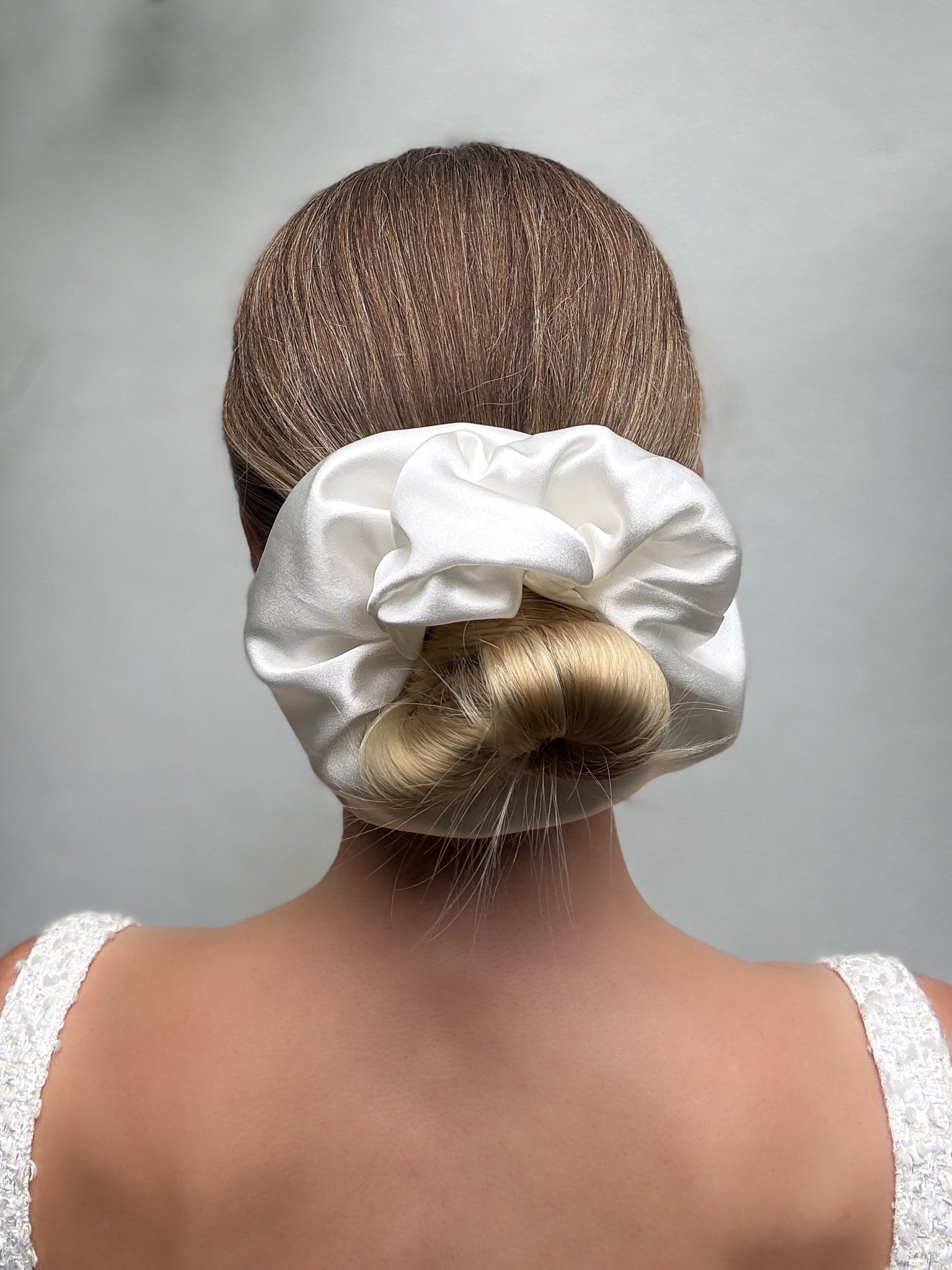 White satin hair scrunchie on a bun against a gray background