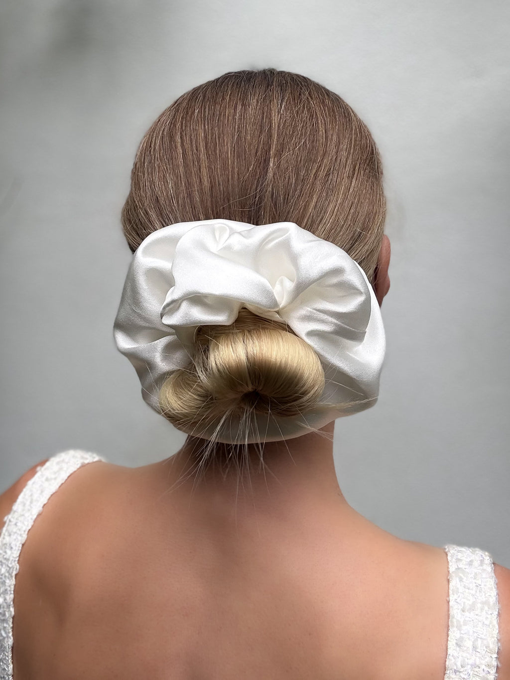 White satin hair scrunchie on a bun against a neutral background