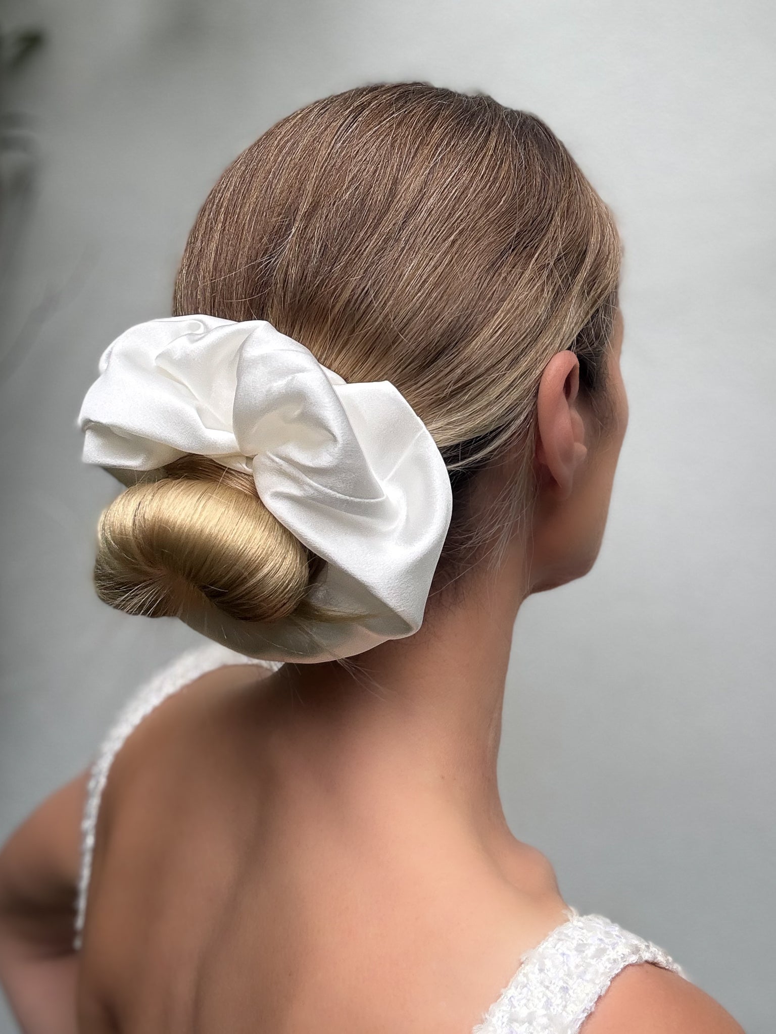 Woman with a styled hair bun using a white scrunchie on a plain background