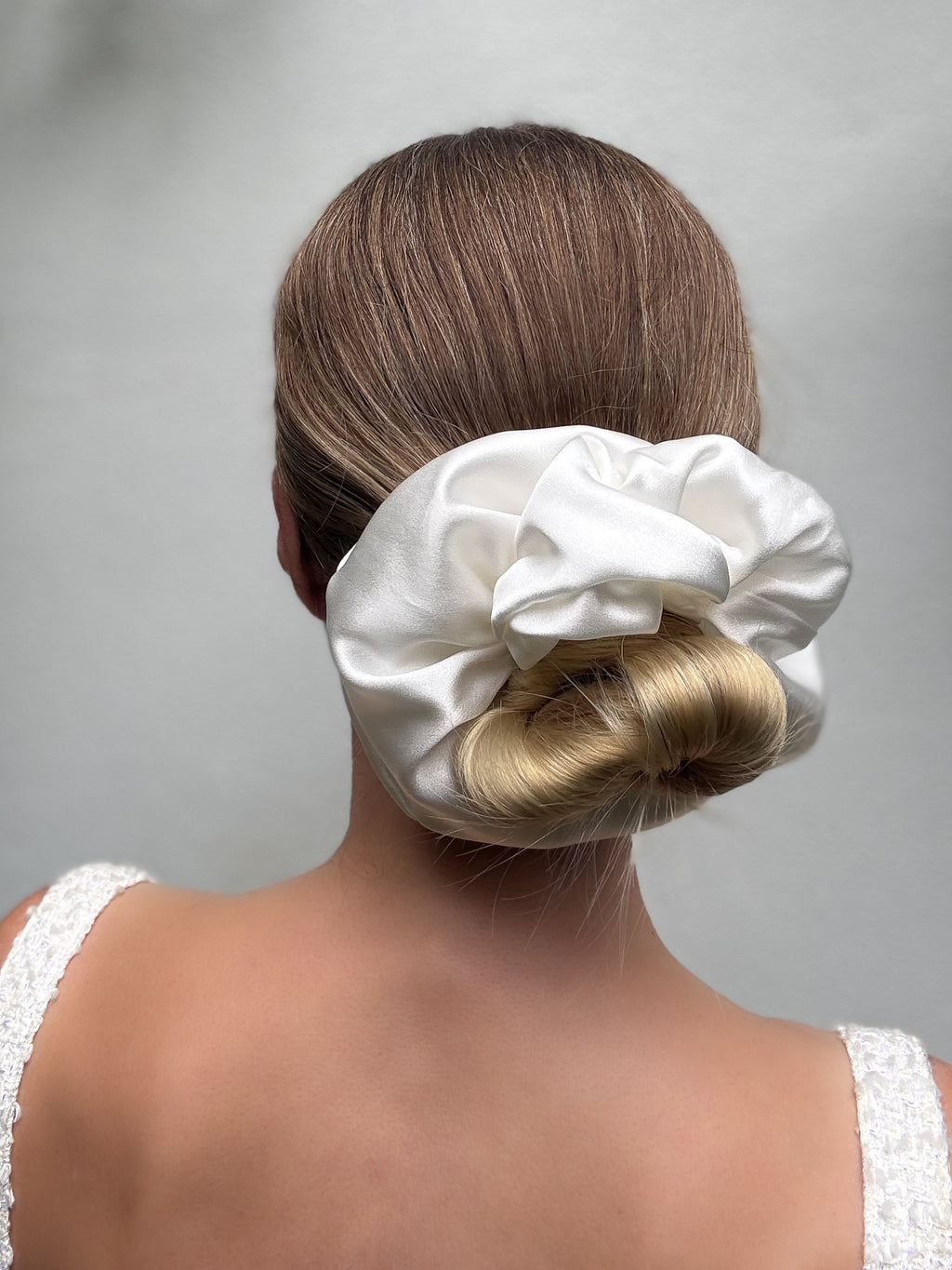 Woman with a white satin scrunchie on her bun against a plain background