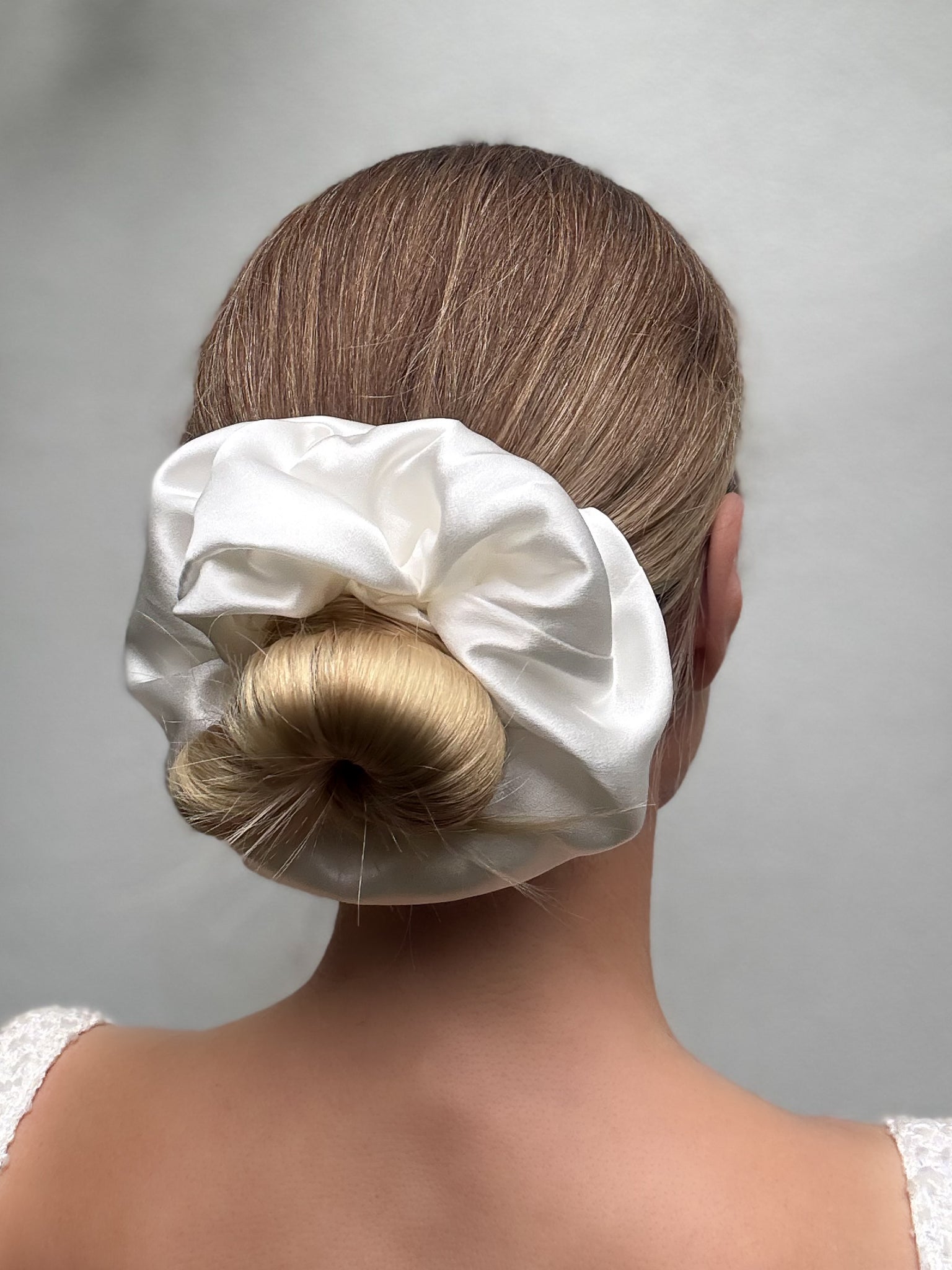 White satin hair scrunchie on a bun against a plain background