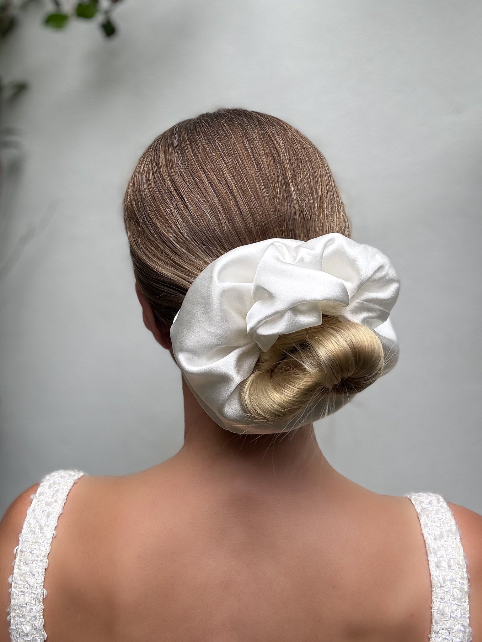 Woman with a white satin scrunchie in her bun against a neutral background