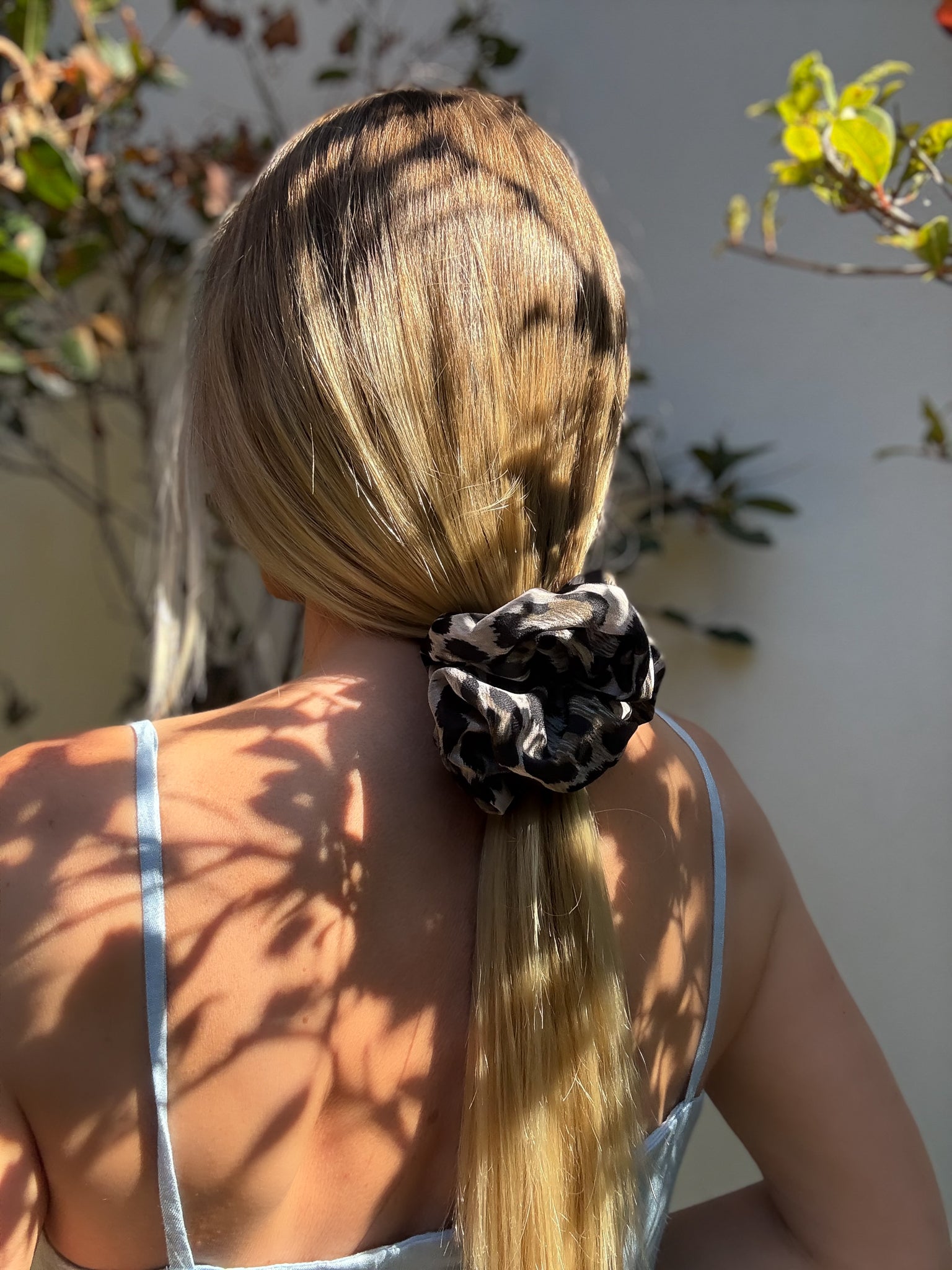Person with long blonde hair tied back with a leopard print scrunchie, standing outdoors.
