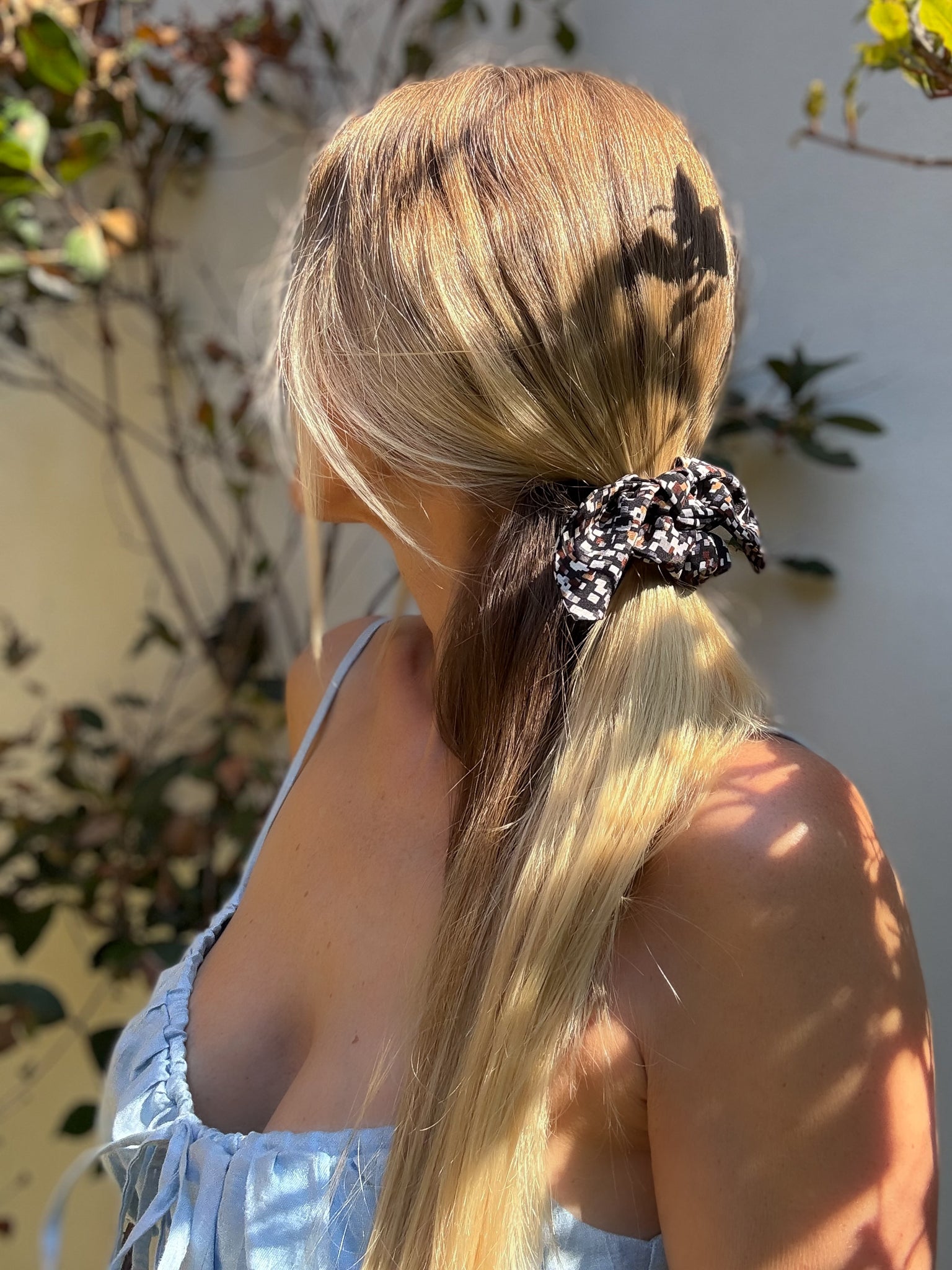 Person with long blonde hair tied with a printed scrunchie outdoors