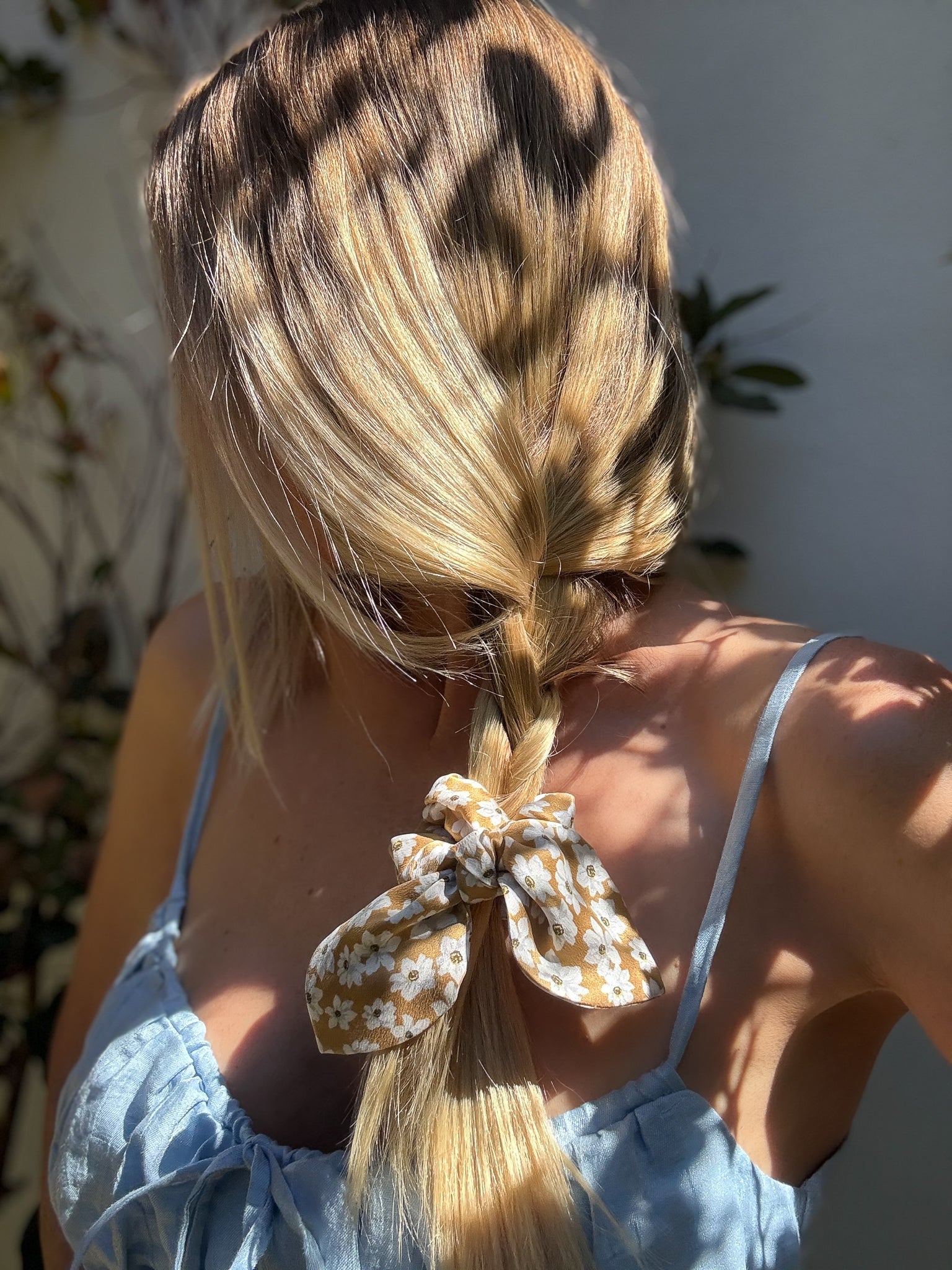 Person with blonde hair styled in a braid with a decorative bow scrunchie, wearing a light blue top.