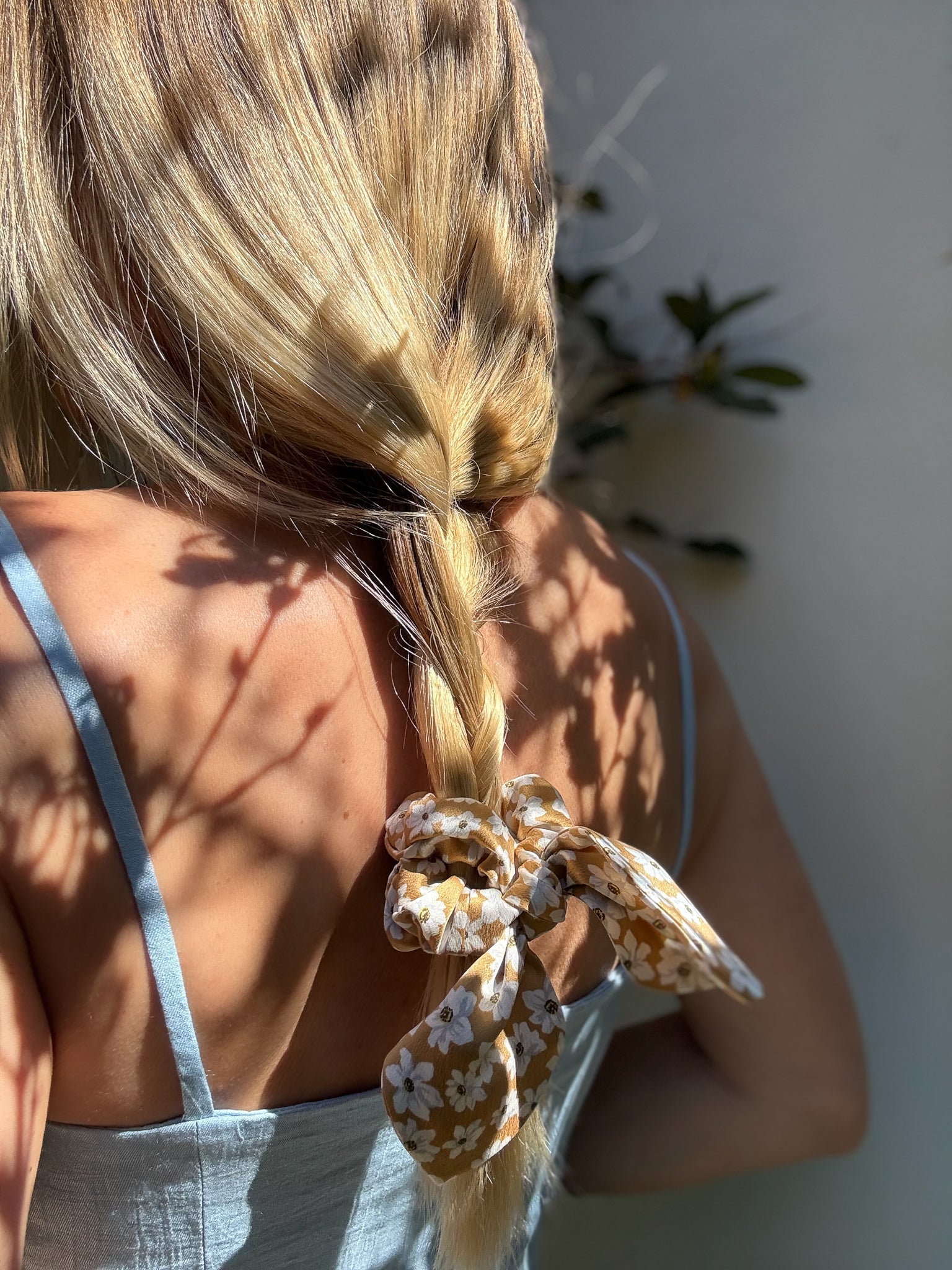 Person with a floral scrunchie in their hair against a neutral background