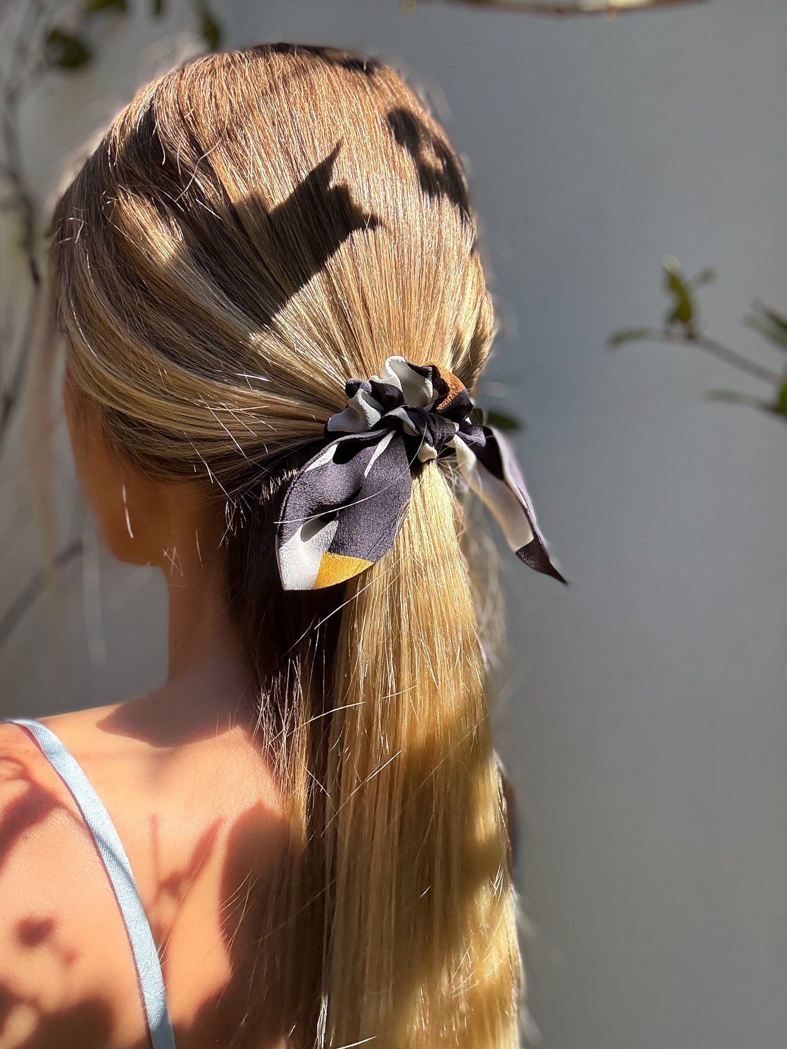 Woman with long blonde hair tied back with a black and white scrunchie against a neutral background