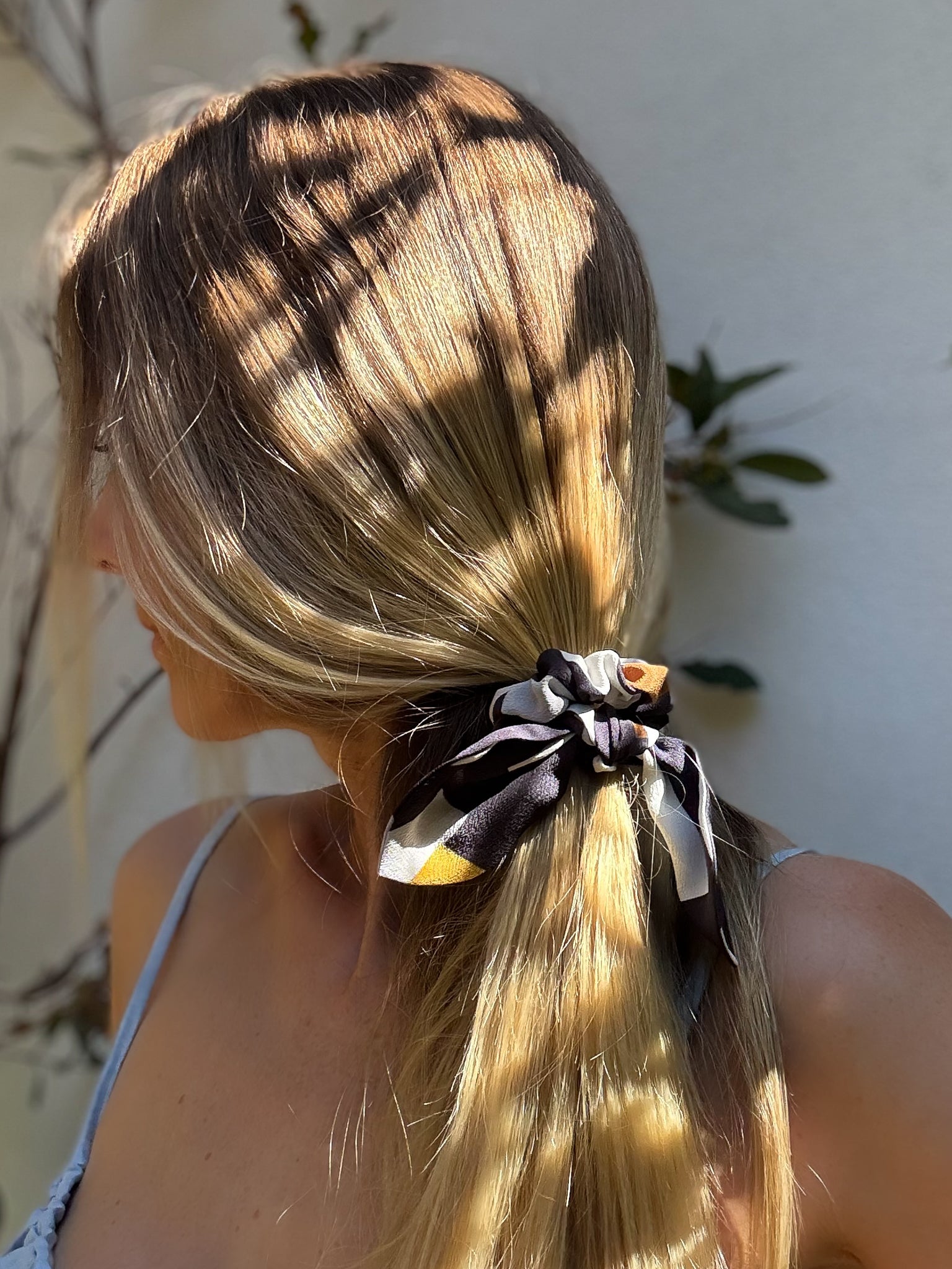 Person with blonde hair tied in a ponytail with a decorative scrunchie, standing outdoors.