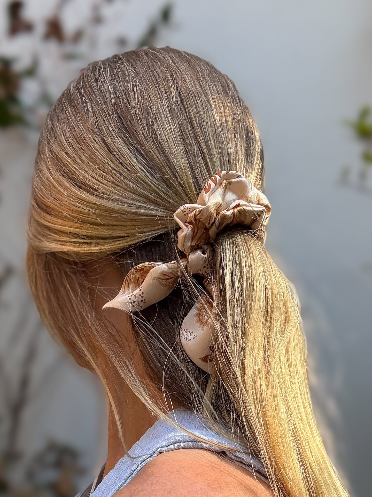 Person with long blonde hair tied back using premium mini hair silk scrunchie against a blurred natural background
